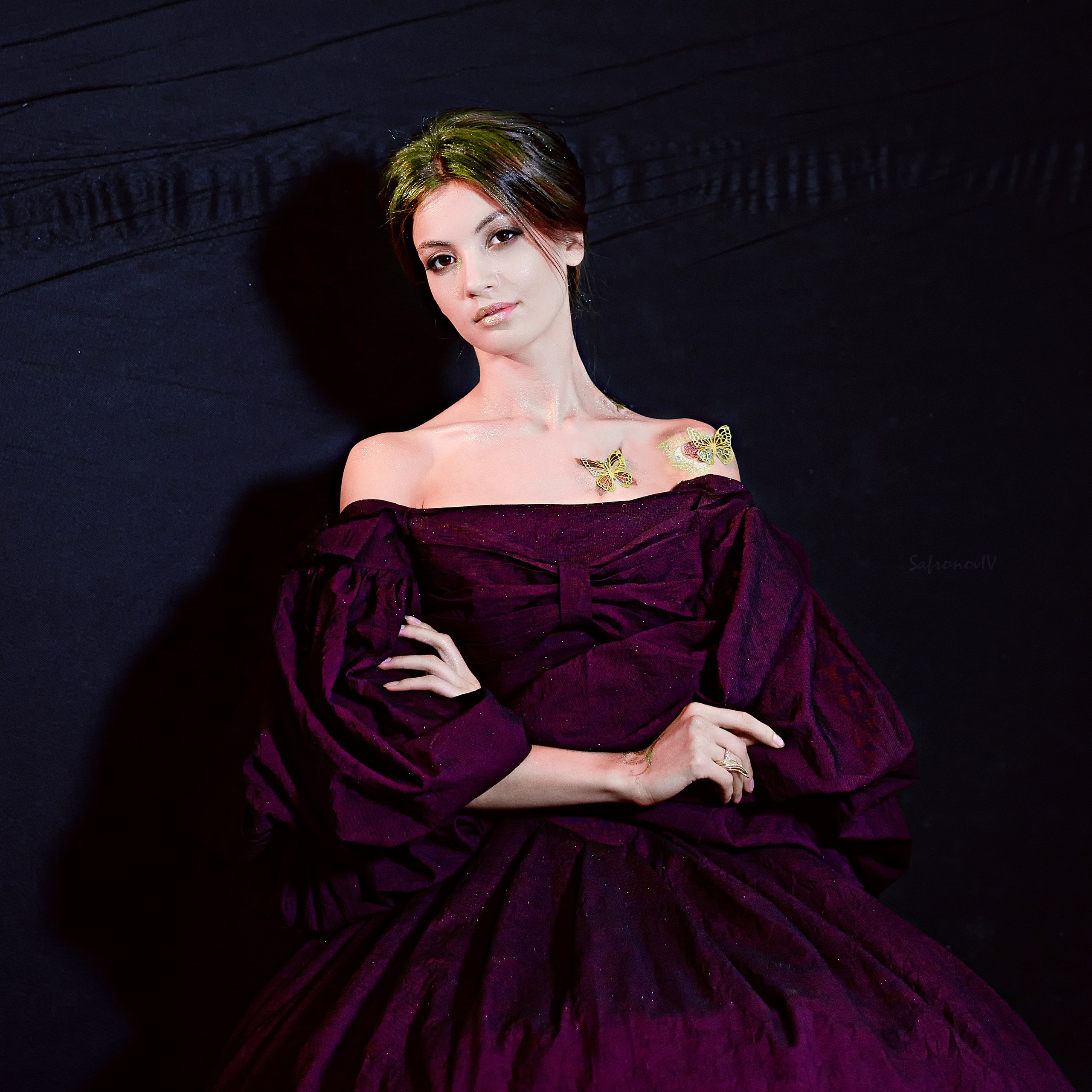 женщина в элегантном бордовом платье с открытыми плечами. Её волосы уложены в аккуратную причёску, а на ключице видны татуировки в виде бабочек. Фон тёмный, что подчёркивает изысканность образа.Заголовок: «Элегантность в каждом движении: портрет в стиле ретро»Ключевые слова: исторические платья, викторианские платья, портрет, бабочки, татуировки, фотосессия, фотограф Сафронов Иван, Москва.