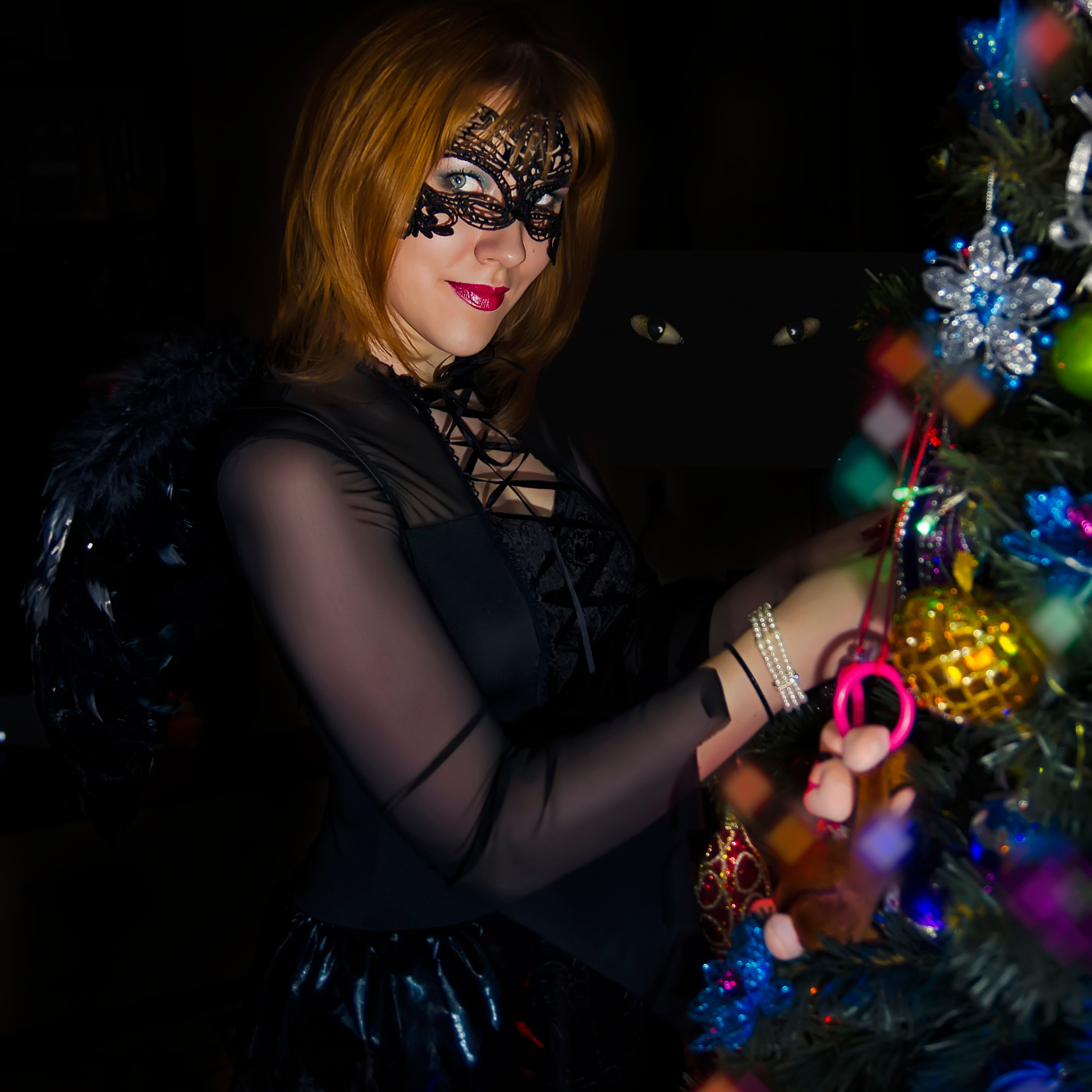Девушка в облике черного ангела стоит возле новогодней елки