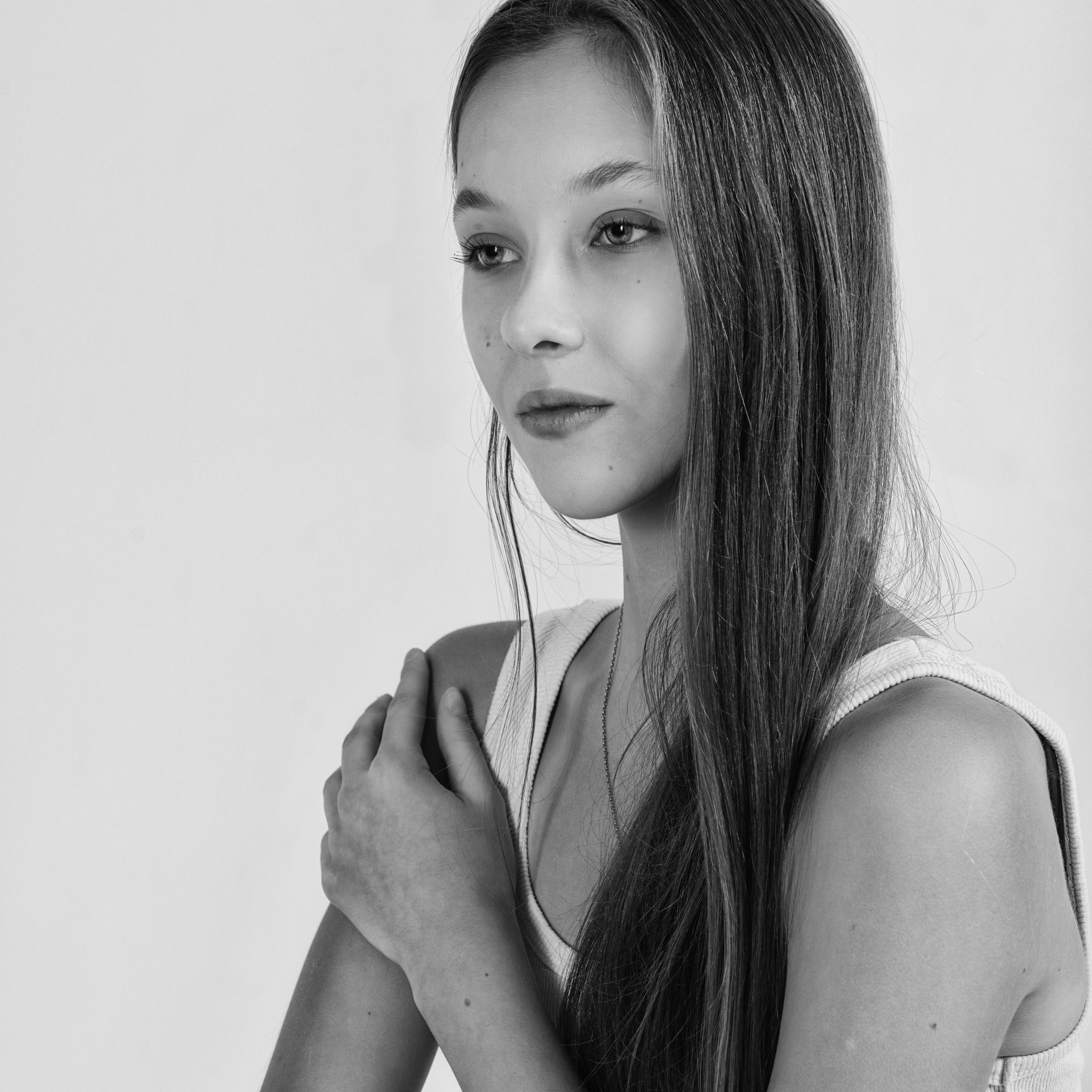 молодая девушка с длинными прямыми волосами. Она смотрит в сторону, создавая ощущение задумчивости и легкой загадочности. Черно-белая гамма подчеркивает текстуру волос и мягкость черт лица. Фон нейтральный, что позволяет сосредоточить внимание на модели.Заголовок: «Загадочный взгляд»Ключевые слова: портрет, черно-белая фотография, девушка, задумчивость, стиль, фотограф Сафронов Иван, Москва