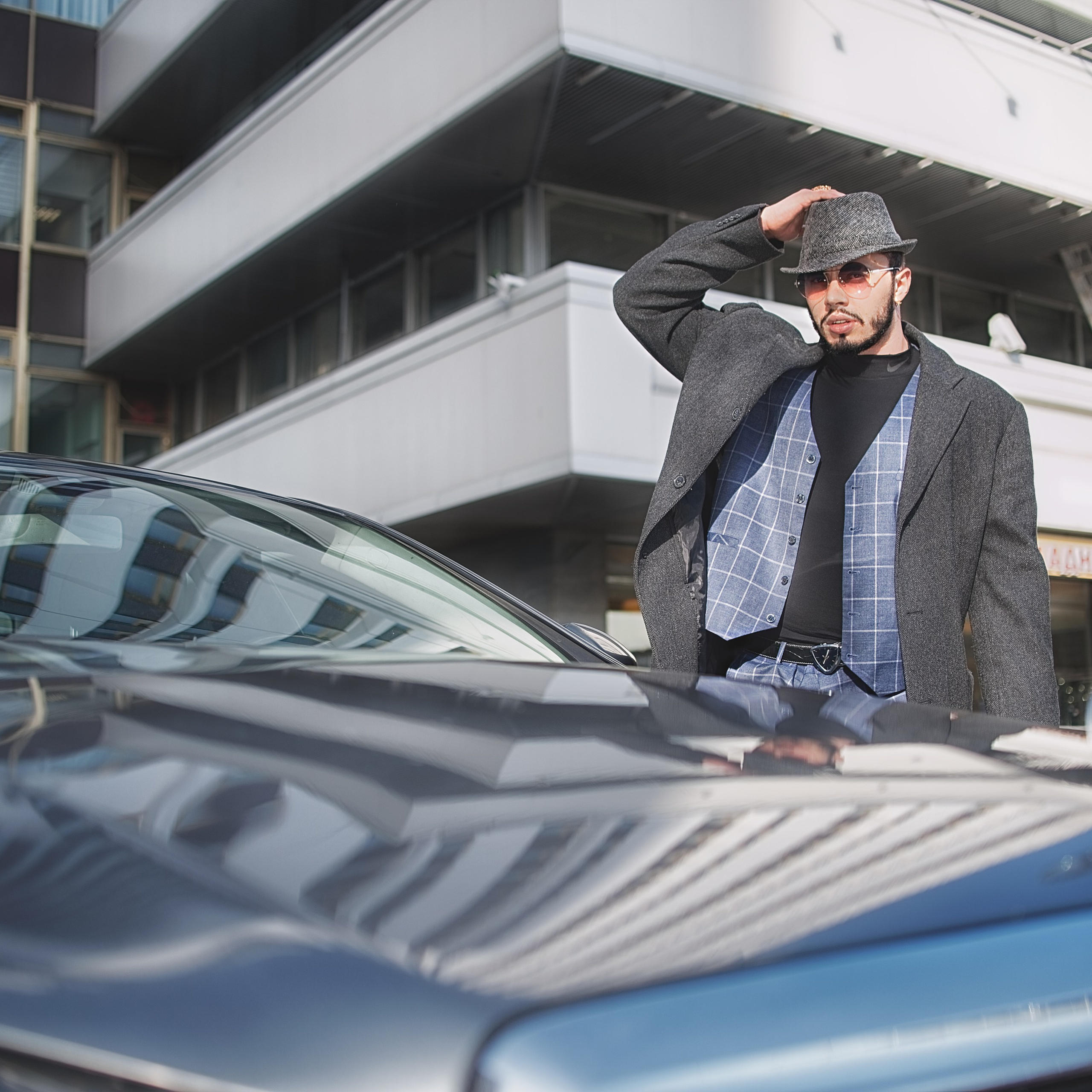 Мужчина в пальто и костюме снимает шляпу возле машины