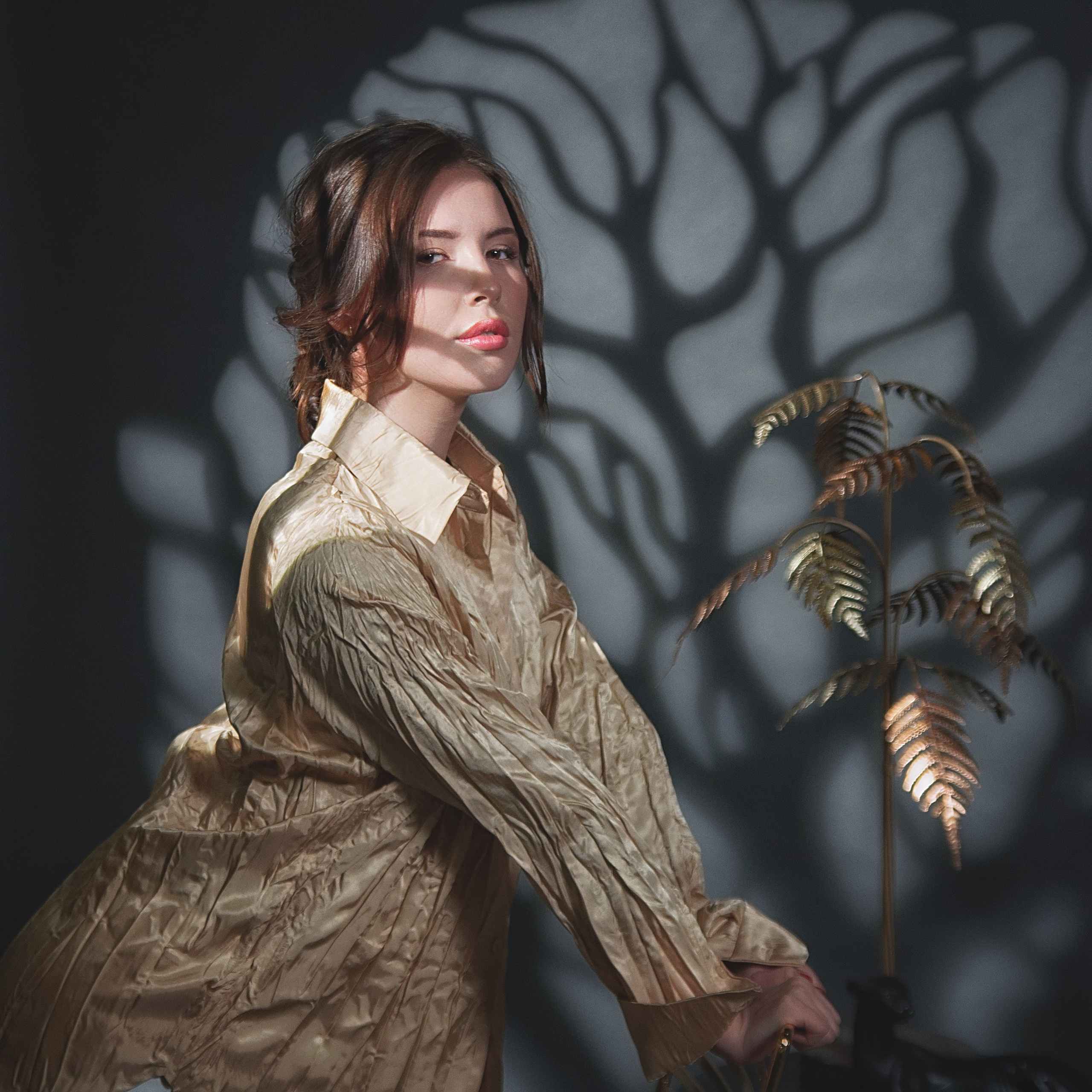 Девушка держится за стул, на нее падают тени ветвей