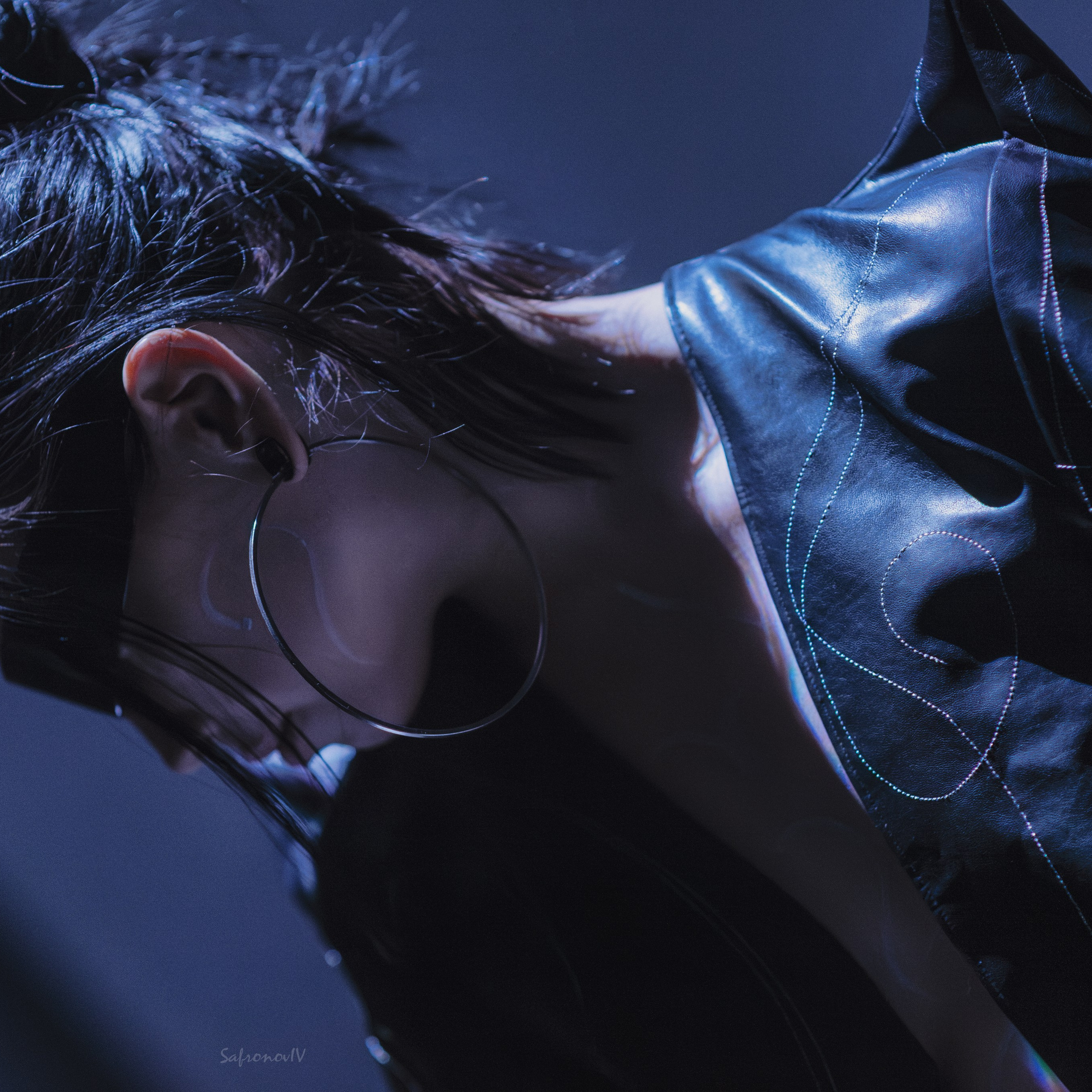 На изображении представлен стильный портрет, выполненный в современном стиле. Человек изображен в динамичном ракурсе, с акцентом на крупные серьги-кольца и блестящую черную кожаную одежду. Свет падает на лицо и ткань, создавая игру теней и бликов, что добавляет глубину и драматичность снимку.Ключевые слова: портретный фотограф в Москве, фотограф Сафронов Иван, современный стиль, кожа, серьги, драматический свет, текстура, контраст.