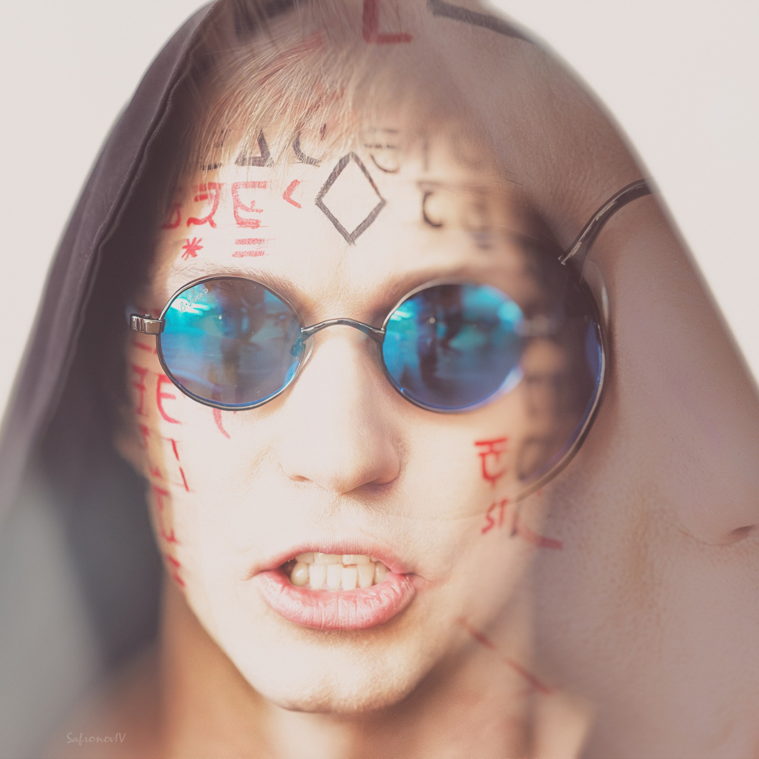 На изображении представлен человек с татуировками на лице, в круглых зеркальных очках и с капюшоном, частично закрывающим лицо. Отражение в очках добавляет глубину и загадочность.Заголовок: «Зеркальный взгляд: искусство и стиль»Ключевые слова: татуировки, лицо, очки, отражение, стиль, мода, портрет, фотограф, Сафронов Иван, Москва, портретная фотография.