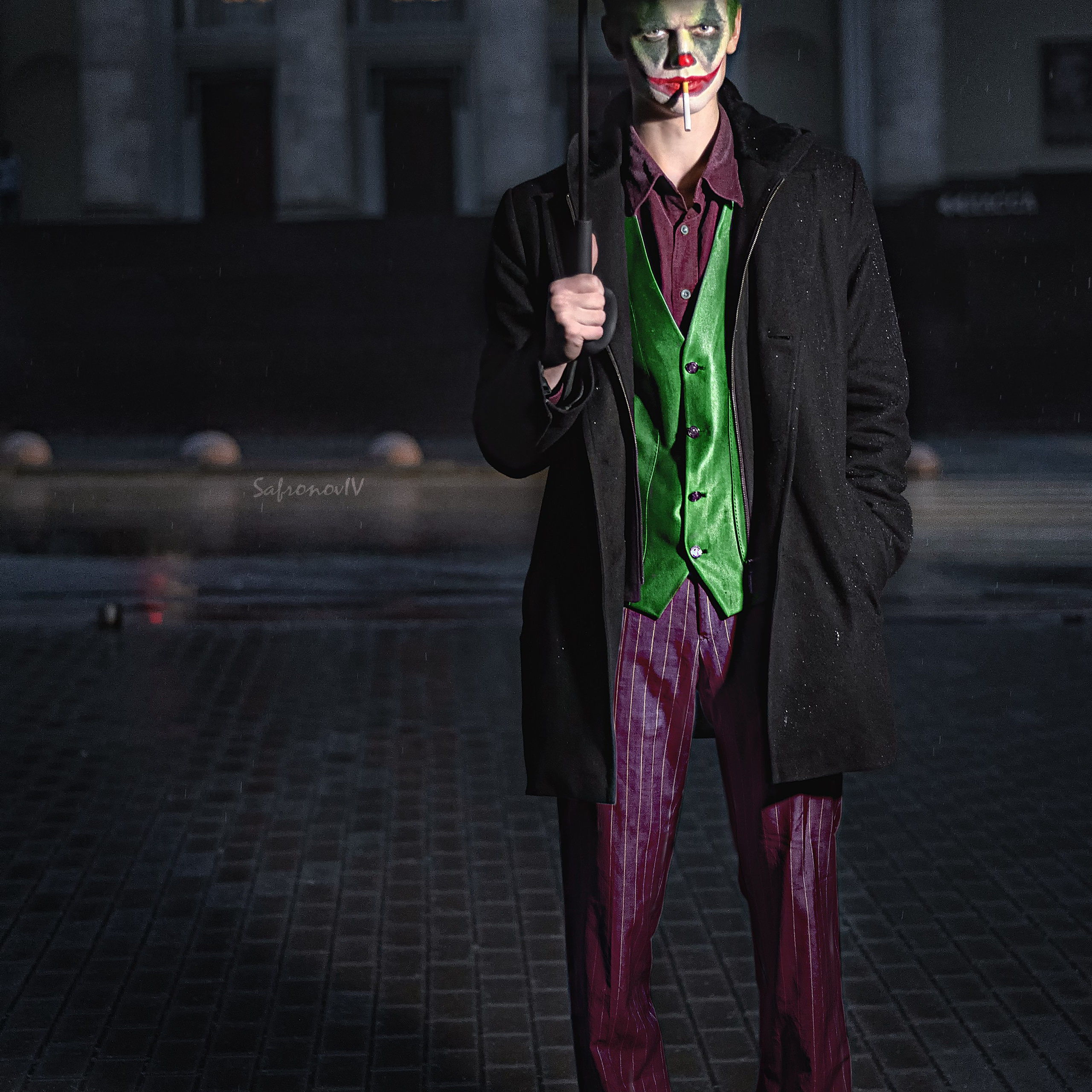 Джокер стоит на темной улице под зонтом