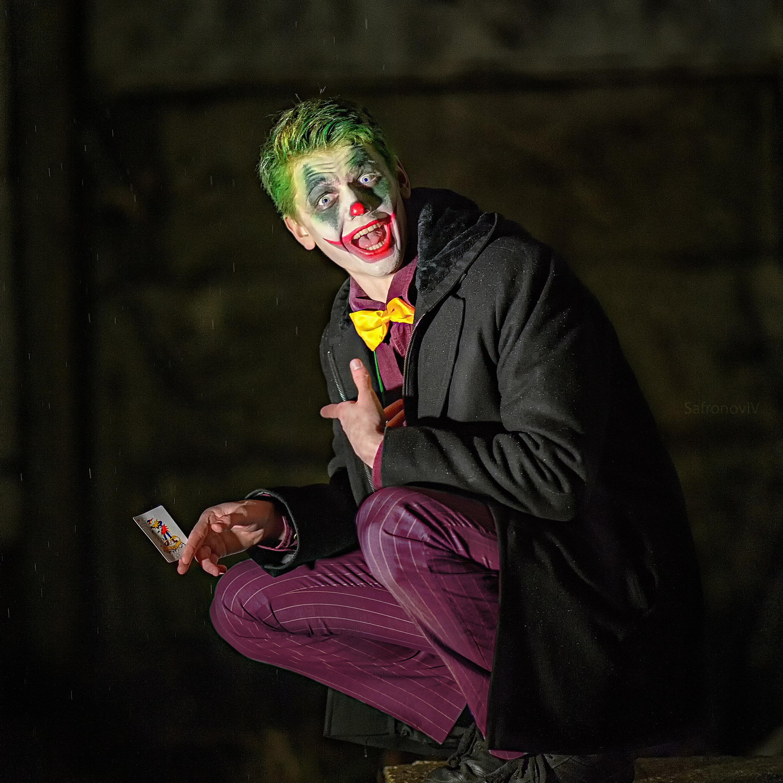Джокер сидит на корточках и показывает на свою карту
