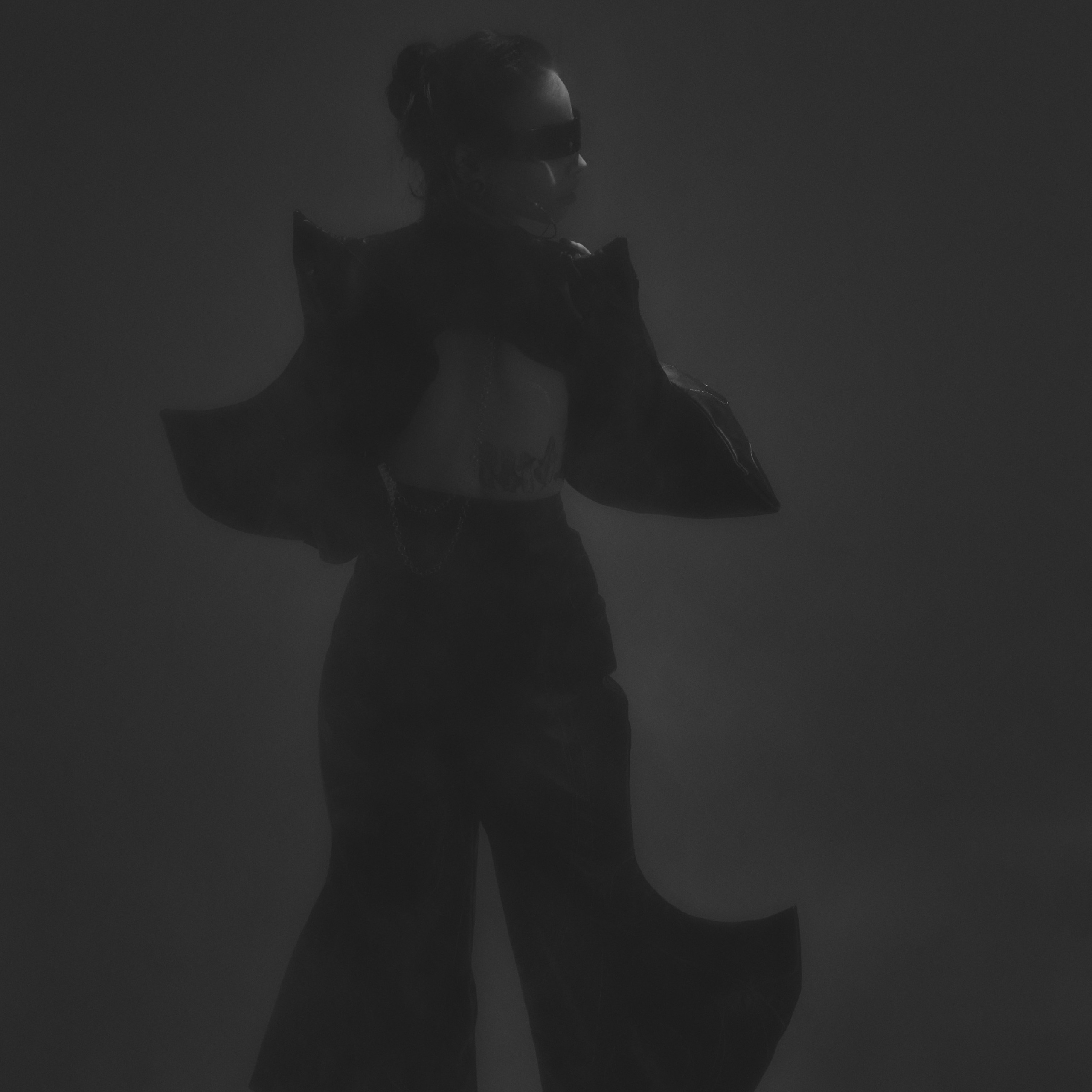 На фотографии изображена девушка в стильном черном наряде, выполненном в готическом стиле. Ее образ дополнен объемными элементами одежды, напоминающими крылья, и высокими сапогами. Свет падает на фигуру, создавая драматический эффект и подчеркивая силуэт. Атмосфера снимка загадочная и утонченная, идеально подходящая для модной фотосессии.Заголовок: «Готическая элегантность: силуэт в свете»Ключевые слова: портретный фотограф в Москве, фотограф Сафронов Иван