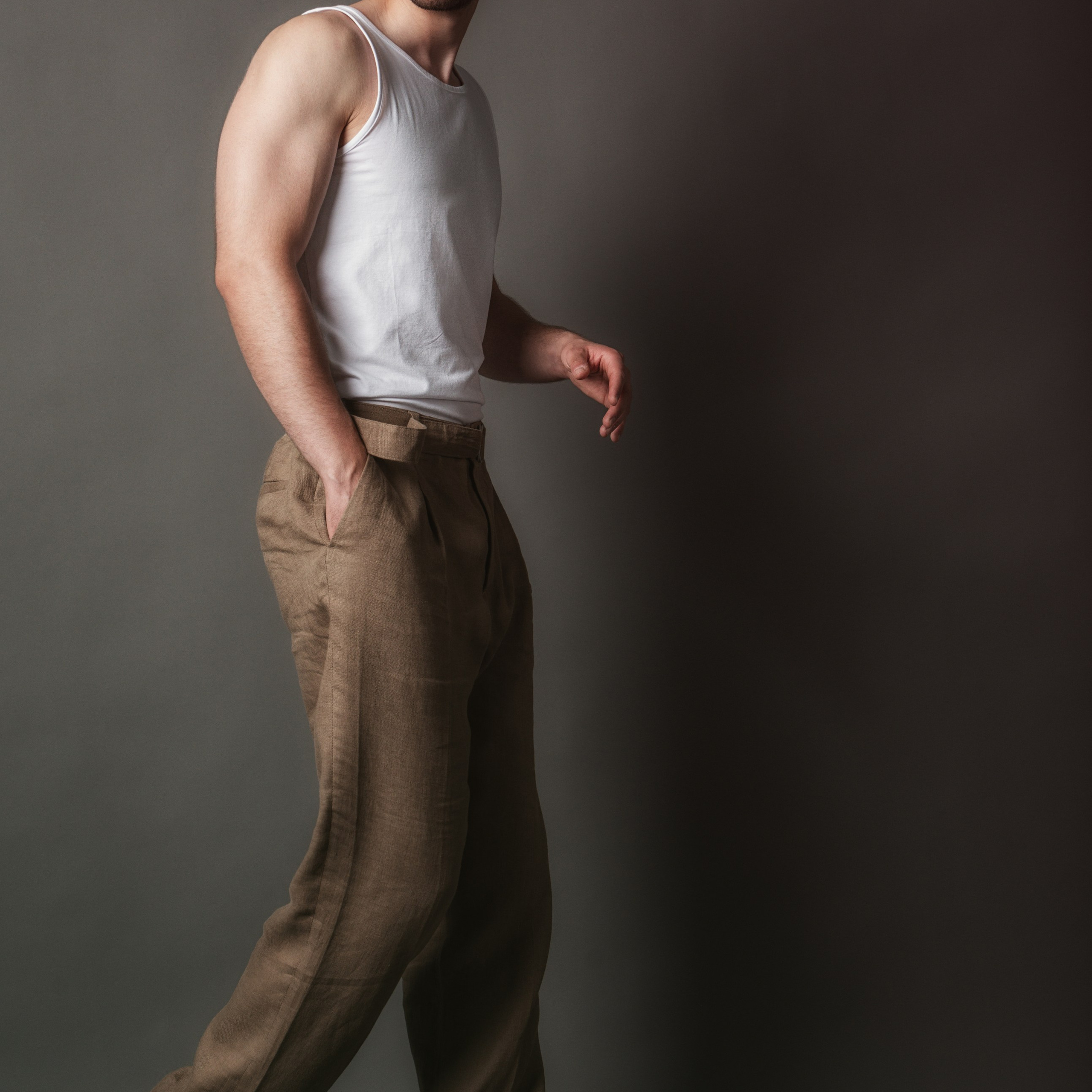 мужчина в белой майке, коричневых льняных брюках и белых кроссовках Nike Air Force 1 Low. Его поза уверенная, взгляд направлен в сторону, что создаёт ощущение силы и решительности. Фон нейтральный, подчёркивающий фигуру и стиль модели.Заголовок: «Сила и решимость»Ключевые слова: портрет, мужская майка, льняные брюки, кроссовки Nike Air Force 1, фотограф Сафронов Иван, Москва.