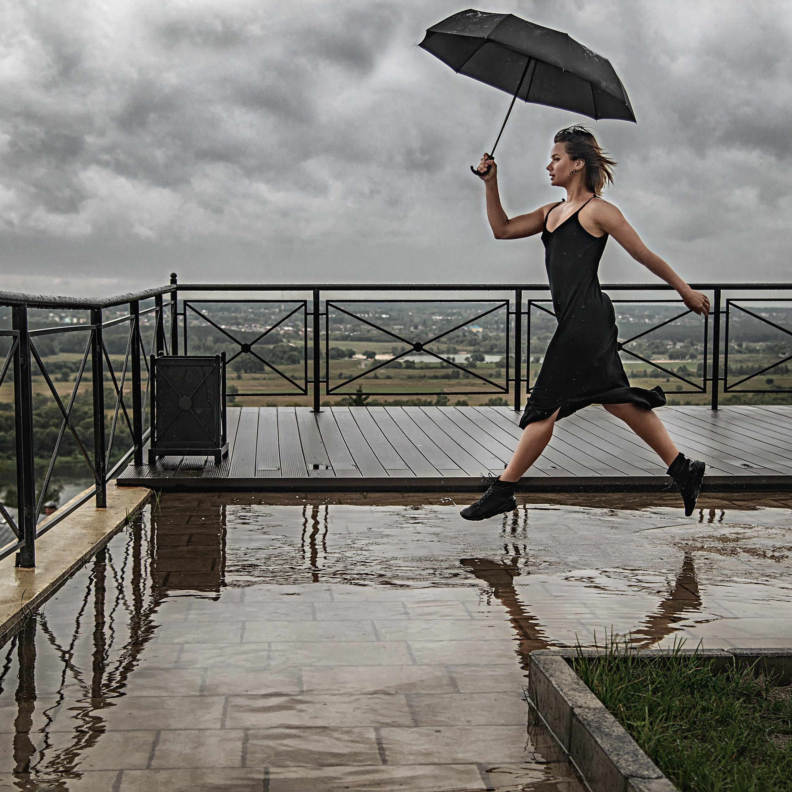 Девушка в черном платье прыгает по лужам