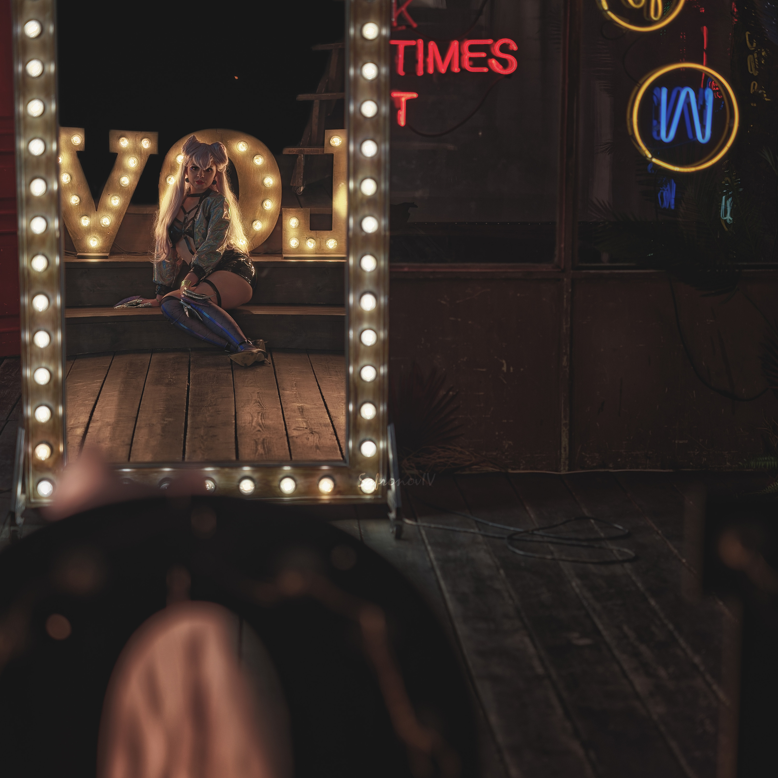 девушка, подсвечиваемая лампами, смотрит в зеркало. отражение девушки в полный рост