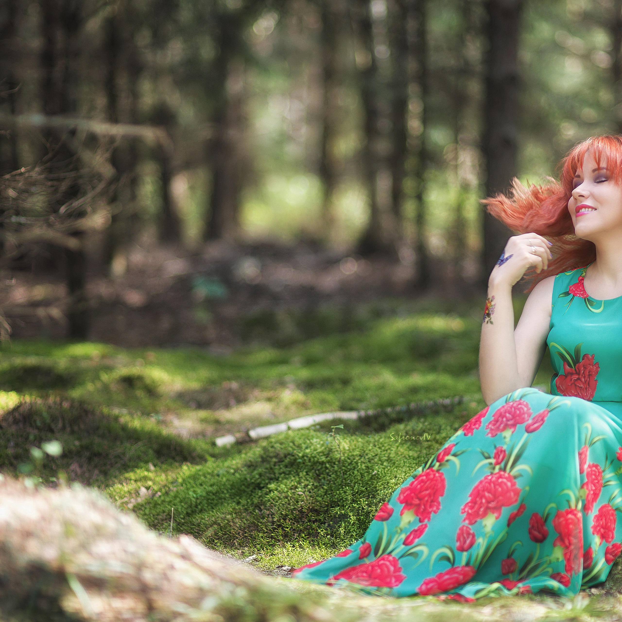 Рыжая девушка в зеленом платье сидит на мху
