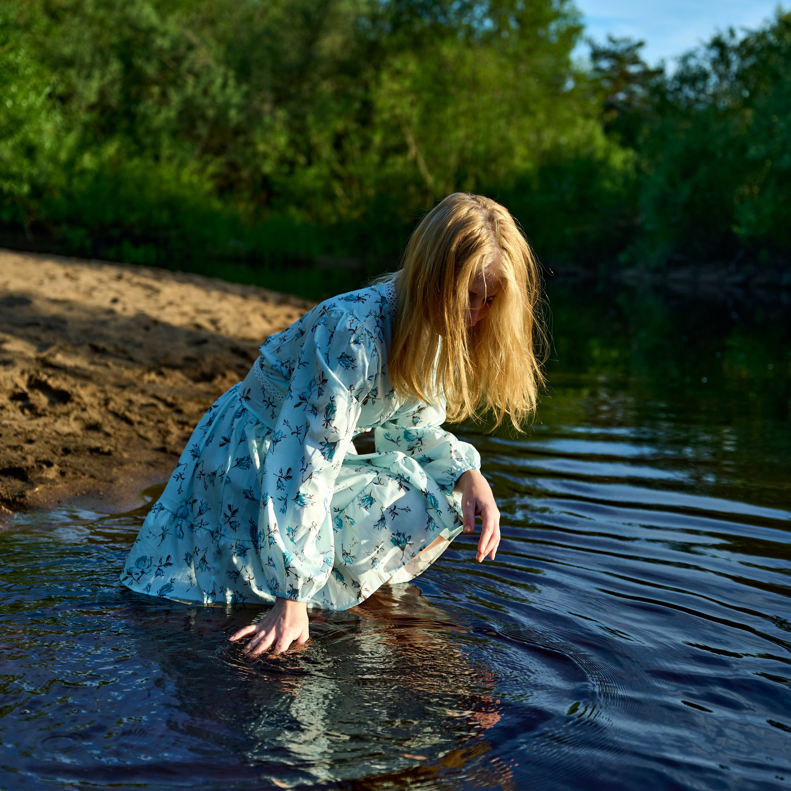 Приседает у воды, касается реки рукой