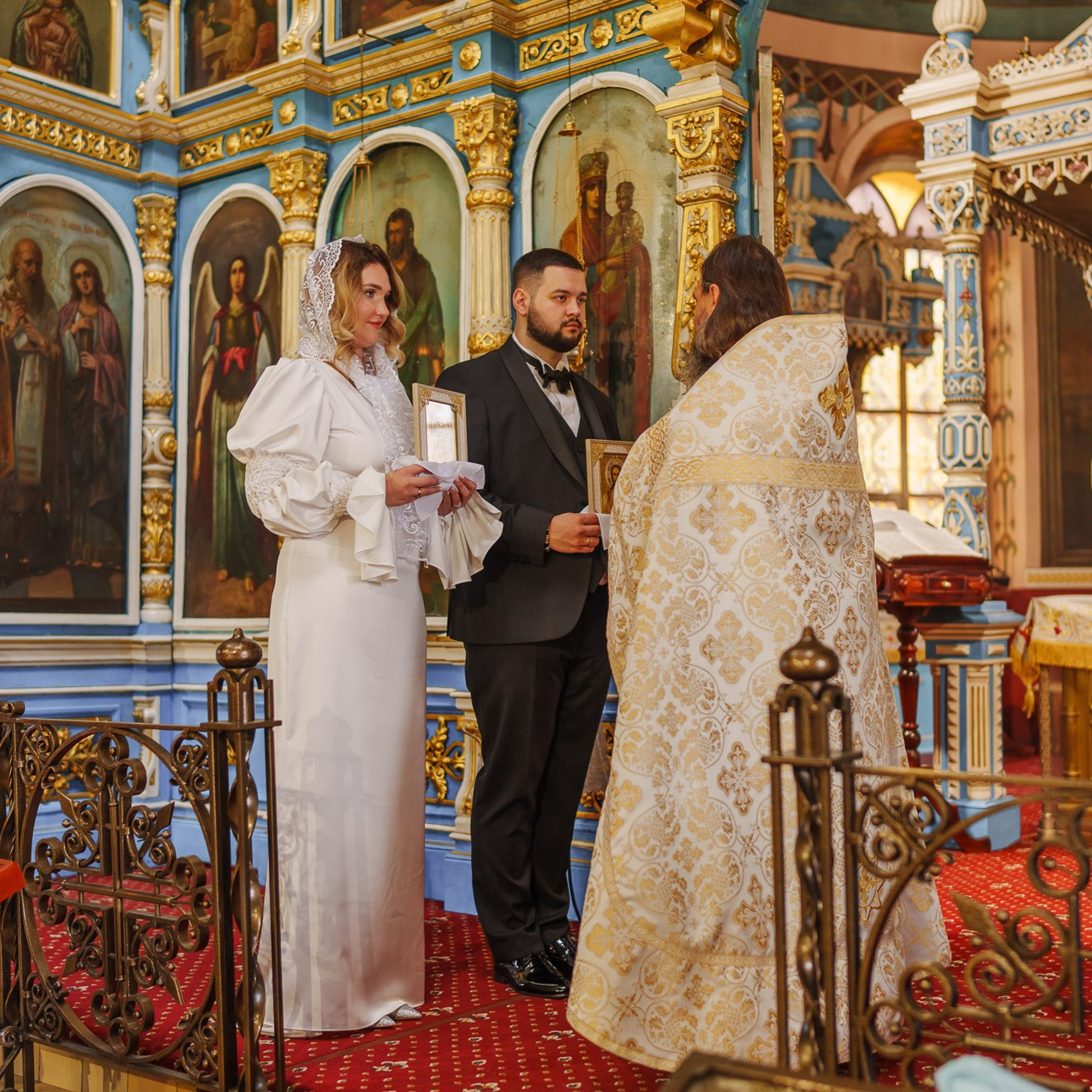 Священник и молодожёны у иконостаса во время православного венчания