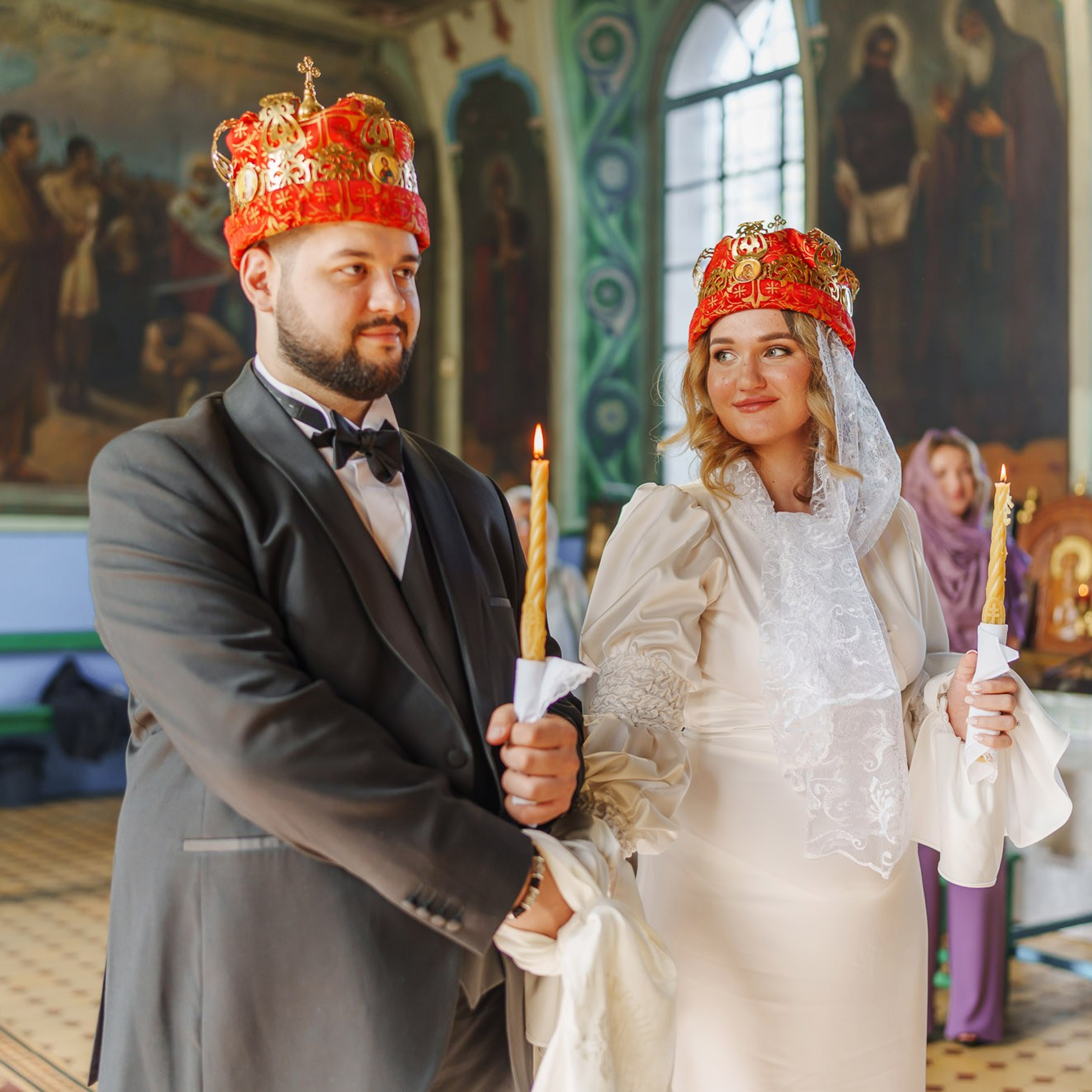 Молодожёны в венцах держатся за руки во время православного венчания