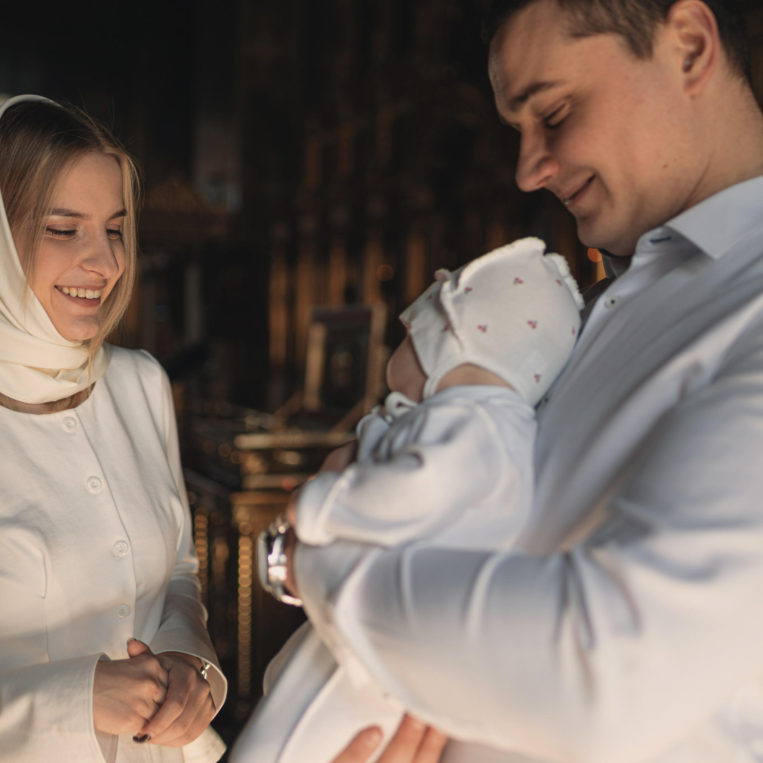 Счастливые родители с малышом во время Таинства Крещения.