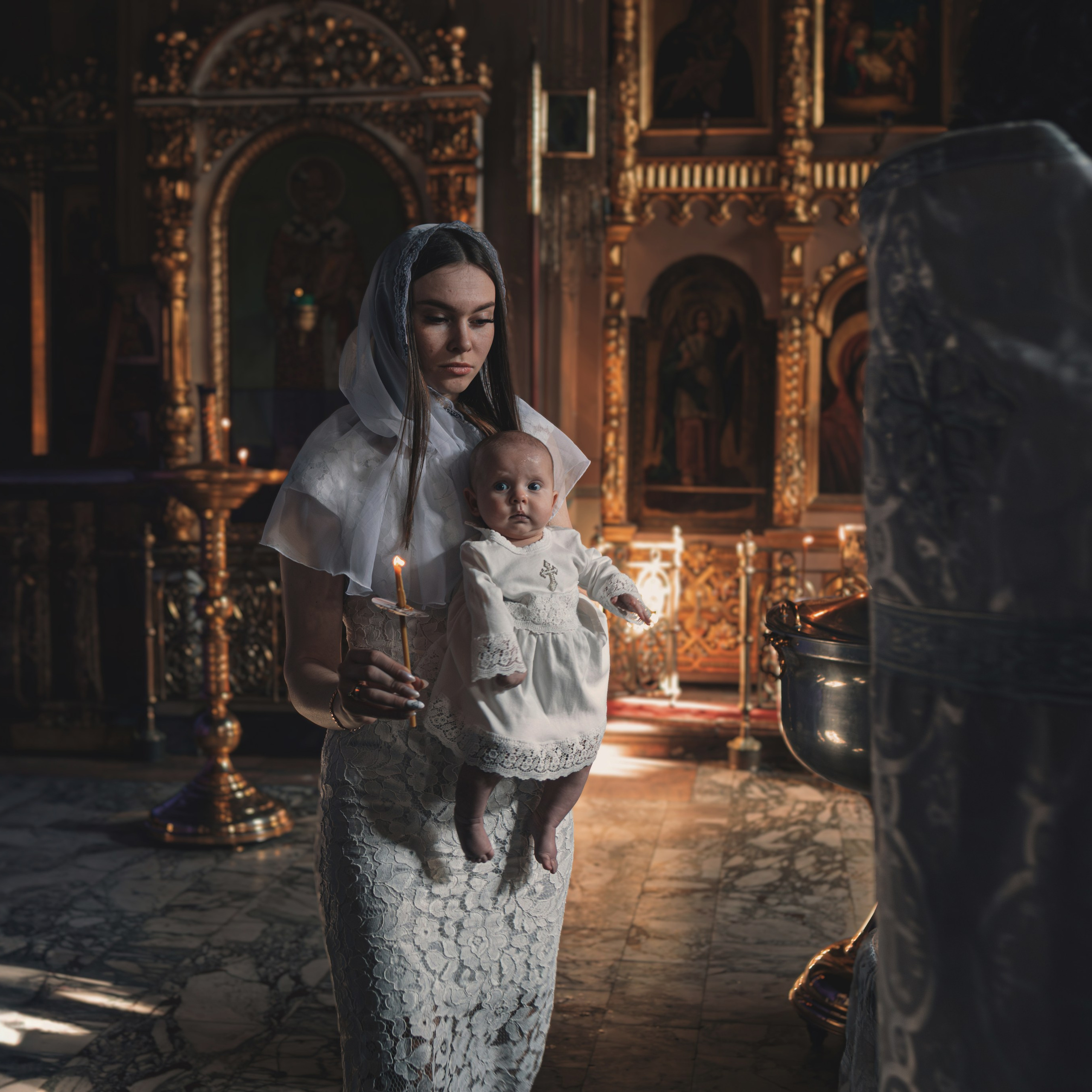 Тёплый кадр Крещения: крёстная держит малыша на руках у алтаря.