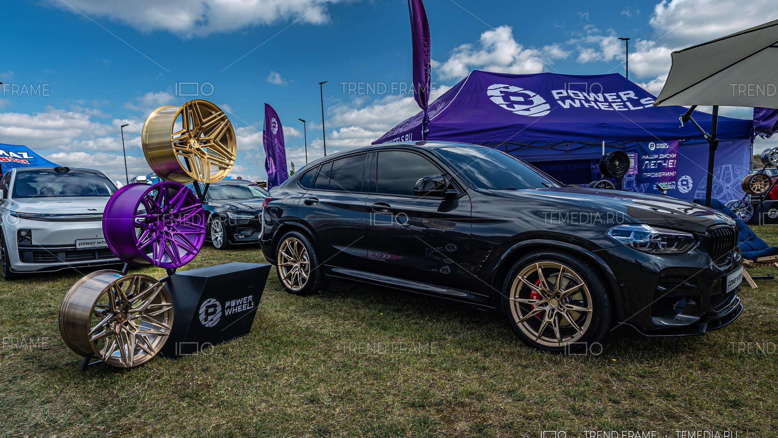 Стенд Power Wheels на выставке в Москве — три кованых диска в золотистом, фиолетовом и бронзовом цвете, чёрный BMW с дисками PowerWheels и красными суппортами