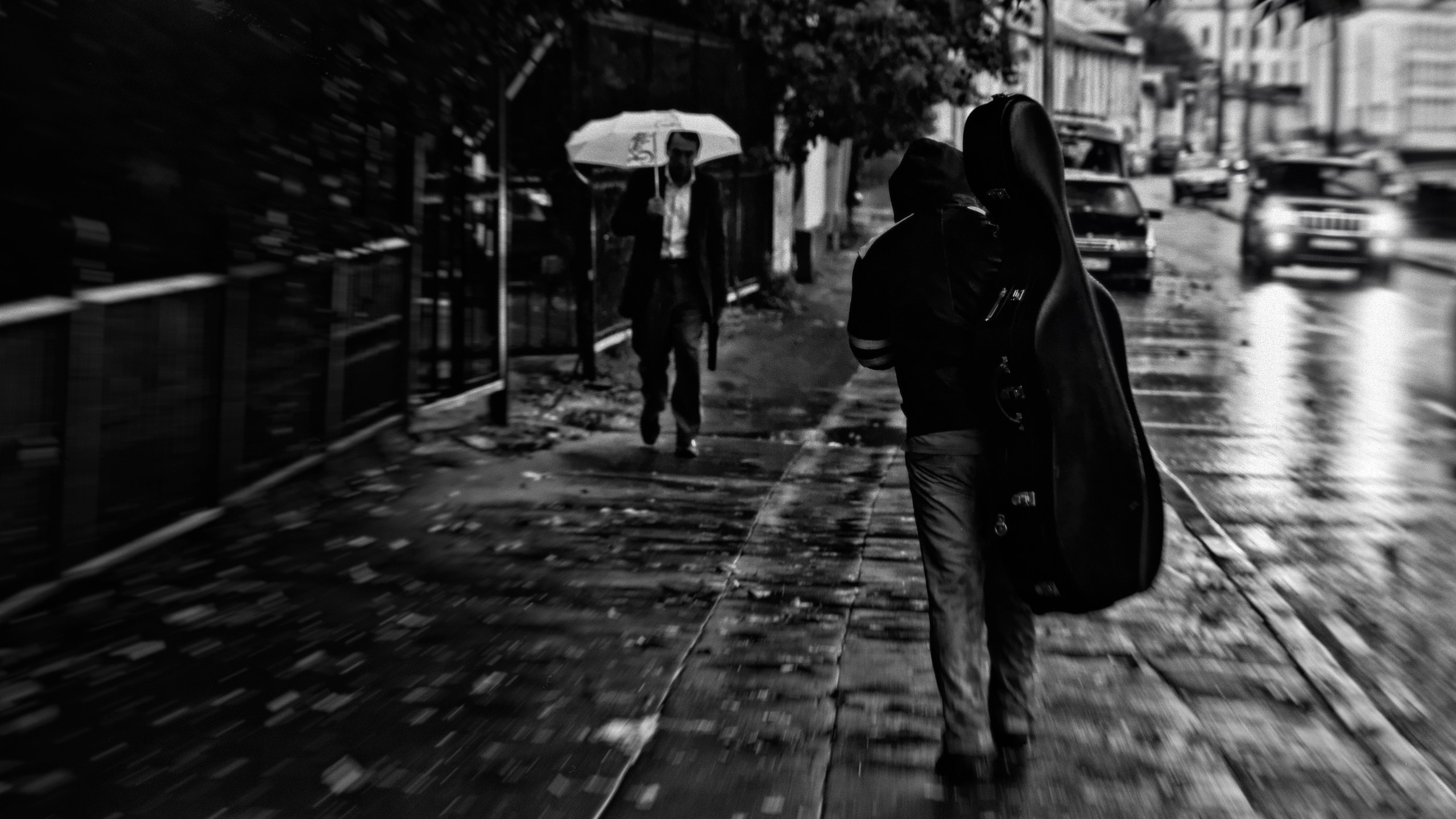 Человек с чехлом для гитары идущий по дождливой улице, размытие движения, человек с зонтом на фоне, атмосферное уличное фото