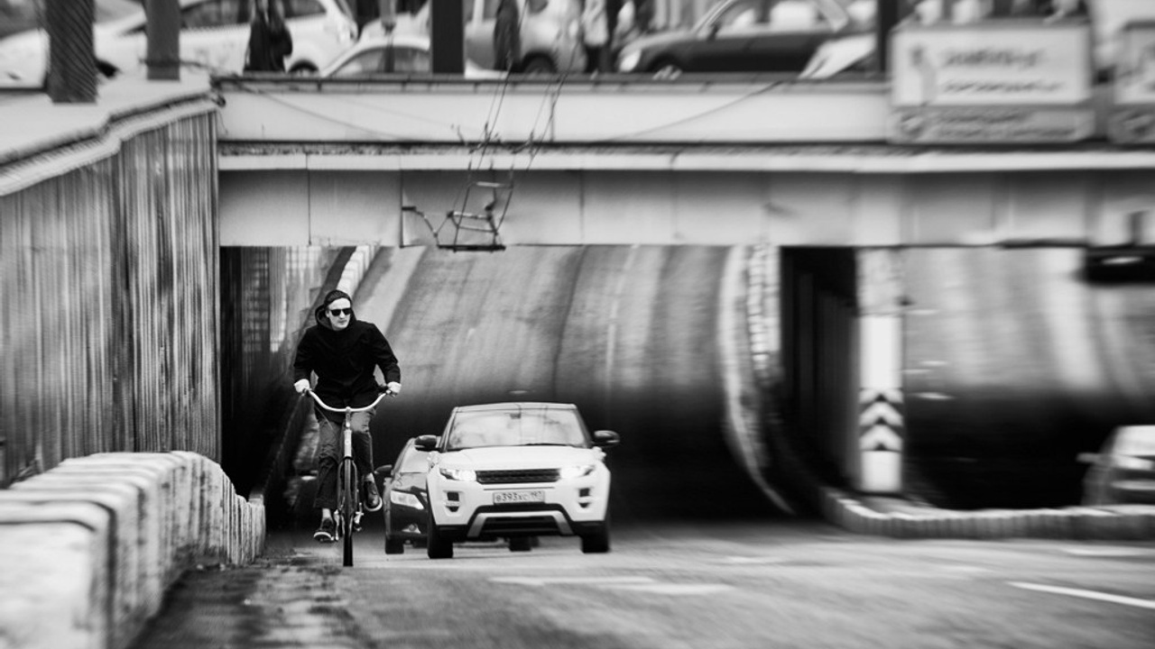 Велосипедист и автомобиль в тоннеле под мостом, эффект размытия движения, черно-белая уличная фотография, городской трафик