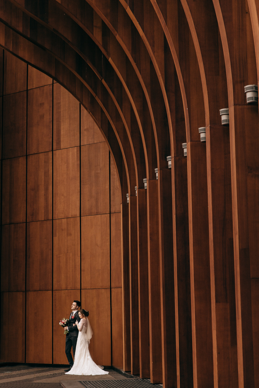 Невеста обнимает жениха на фоне стены концертного зала Barvikha Luxury Village