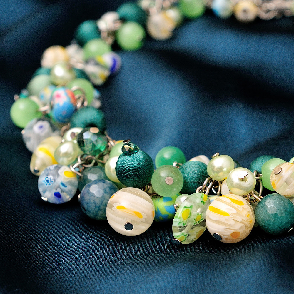 браслет крупным планом из зеленых и персиковых бусин на атласном фоне