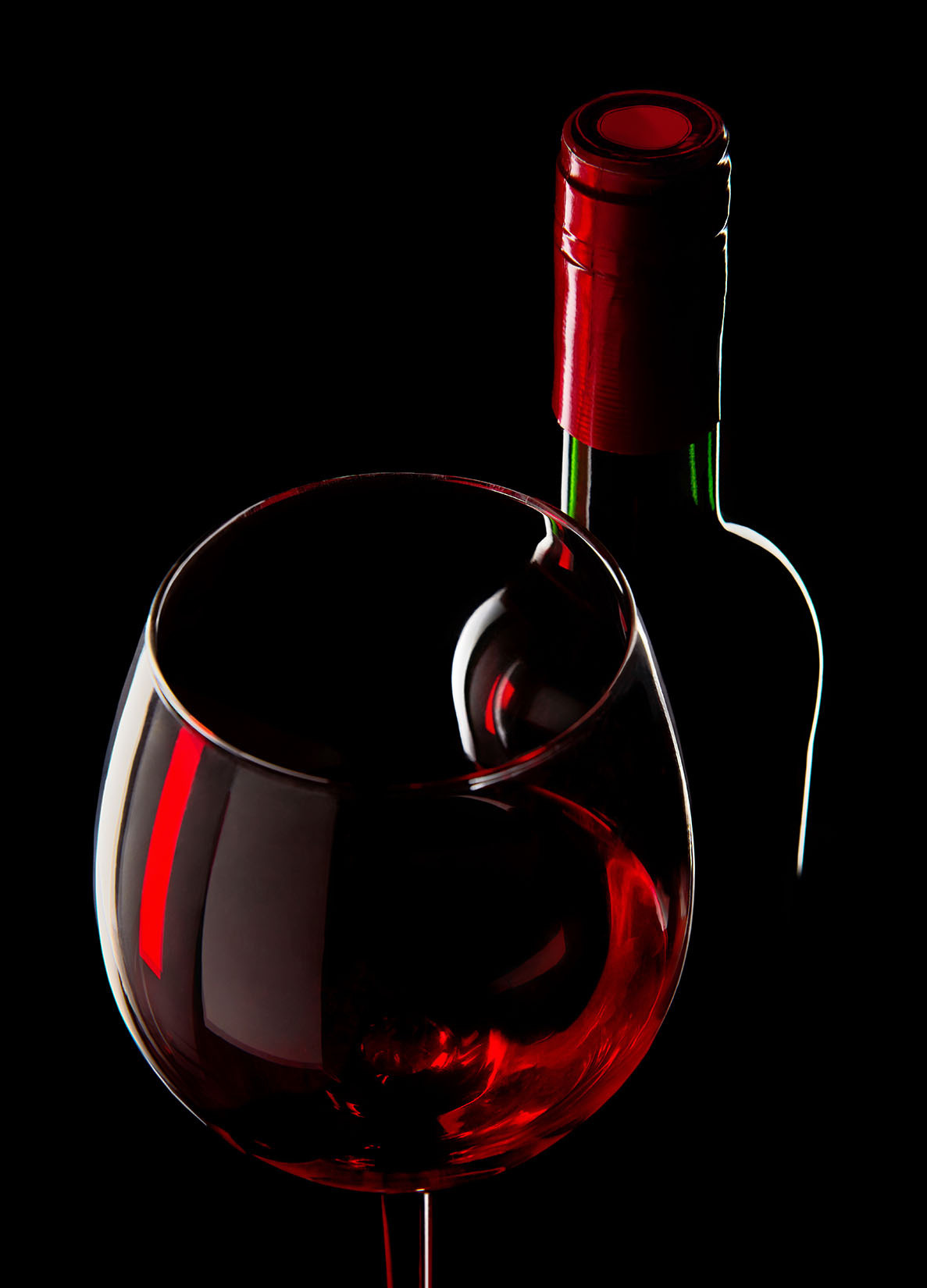 Рекламная фотография на черном фоне - контурный свет и цветные блики на бутылке с фужером вина