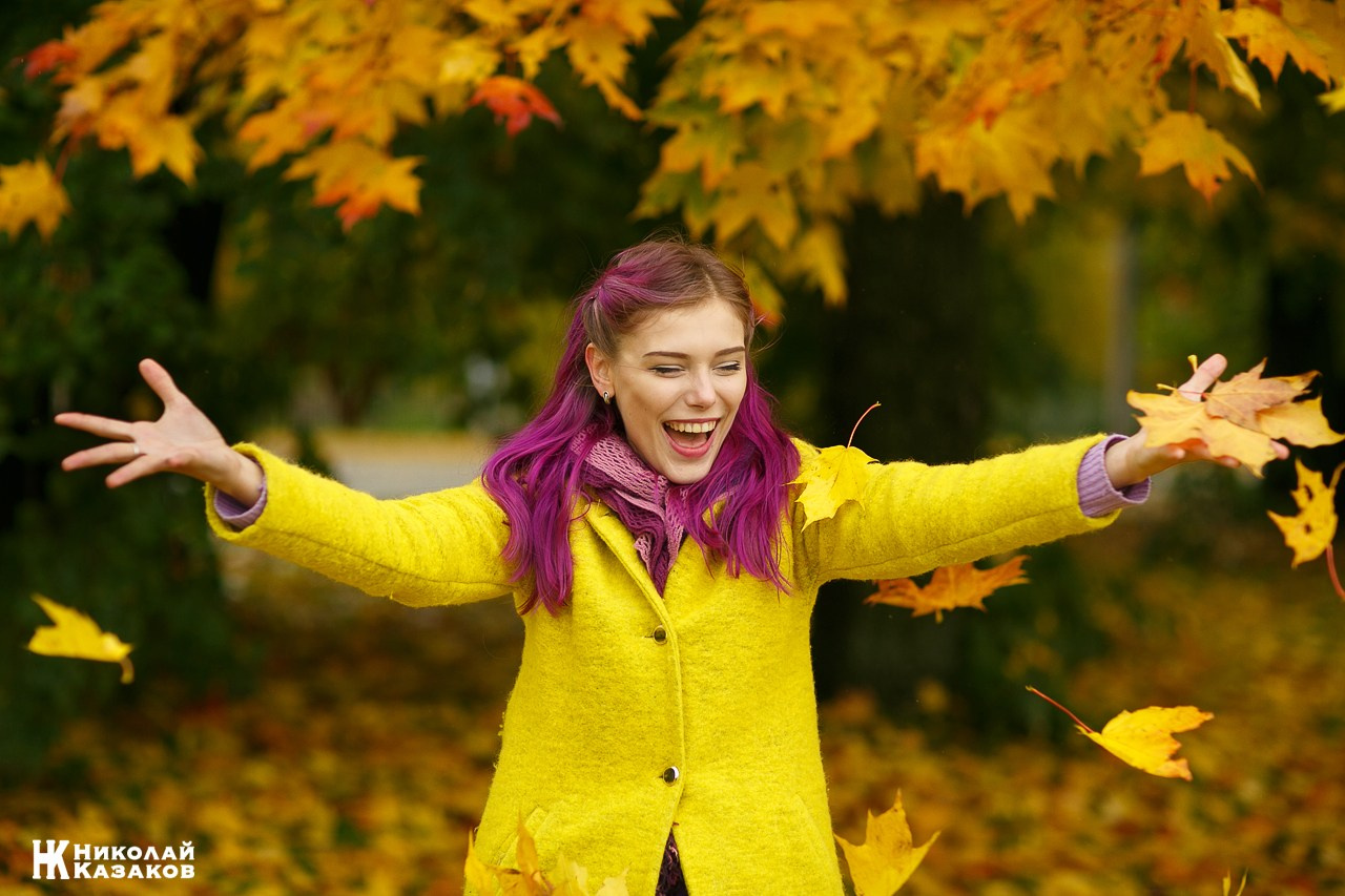 Активная девушка со смехом подбрасывает яркие осенние листья на прогулке