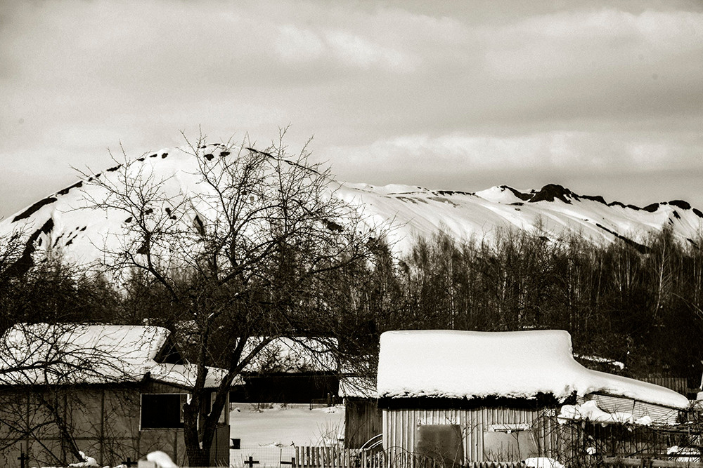 В маленьком поселке под горой жизнь замедляется, и все становится как в детстве - значимым. Все деревья обязательно - большие. Здесь нет мелочей и не нужно наблюдать часов, ведь соседские бабушки в одно и тоже время бредут к обедне. Большая черная собака всегда провожает до крыльца, а следы в глубоких тропинках всегда указывают на своих хозяев. Как и тщательно вытоптанные в снегу цветы говорят о двух маленьких девочках с соседней улицы. Они, конечно, не признаются, но все давно знают, что они договорились приближать весну. Хотя им обычно кто-то мешает, наверное, мальчишки, что строят снеговиков. Я наблюдаю, пропитываюсь неспешностью, становлюсь одним из редких прохожих, который точно знает, что здесь можно жить сердцем, слушать тишину и просто быть.