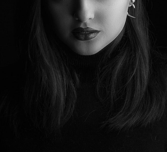 Частичный портрет женщины: губы, подбородок и волосы в мягком свете на тёмном фоне