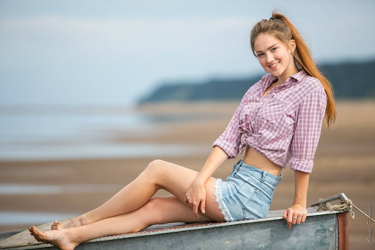 Девушка в шортах позирует на старой лодке на берегу реки