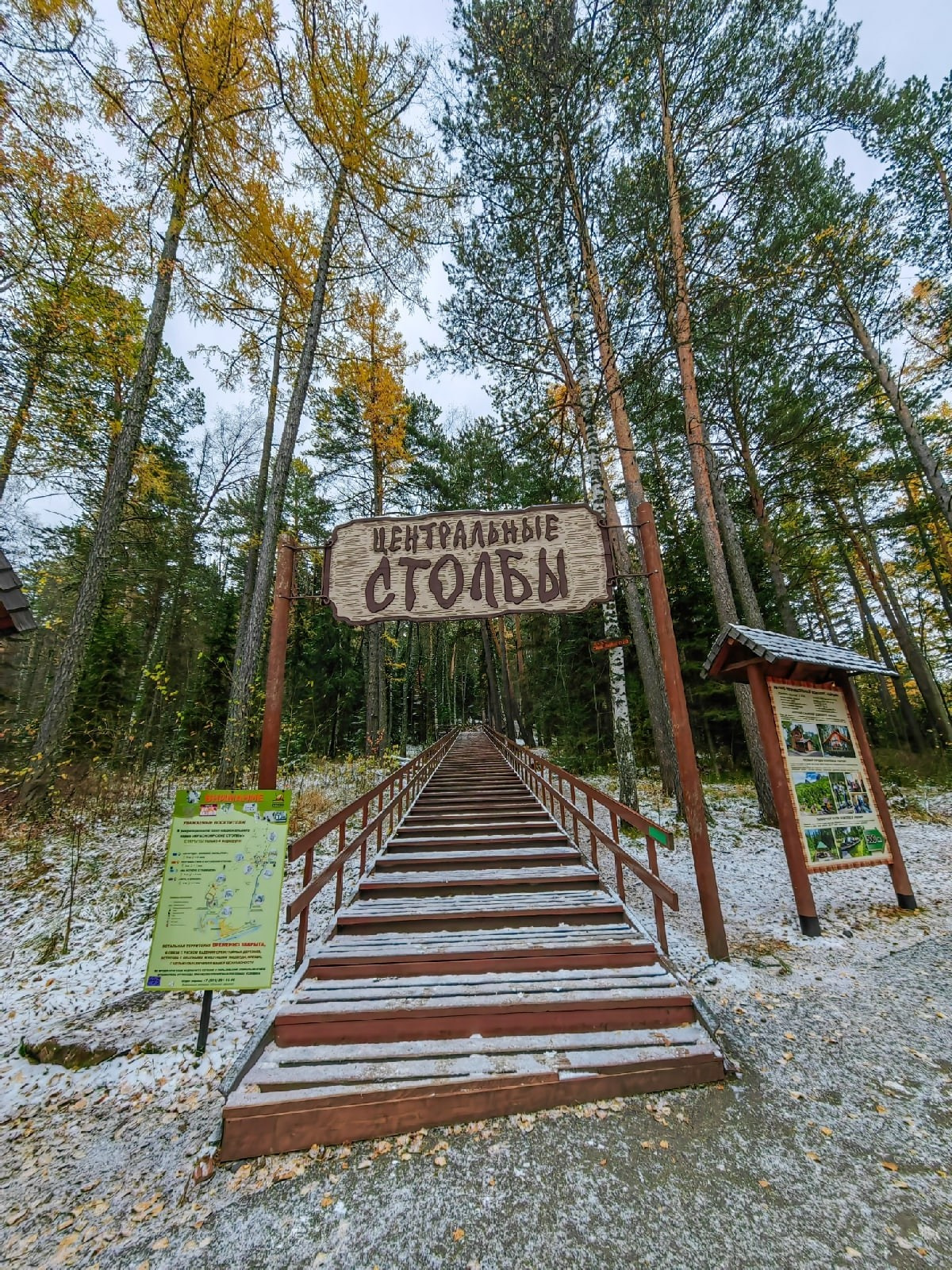 Экскурсия на Центральные Столбы в межсезонье: деревянная лестница под первым снегом уходит в лес, над входом резная вывеска. Индивидуальный тур из Красноярска лучше забронировать заранее, особенно на выходные.