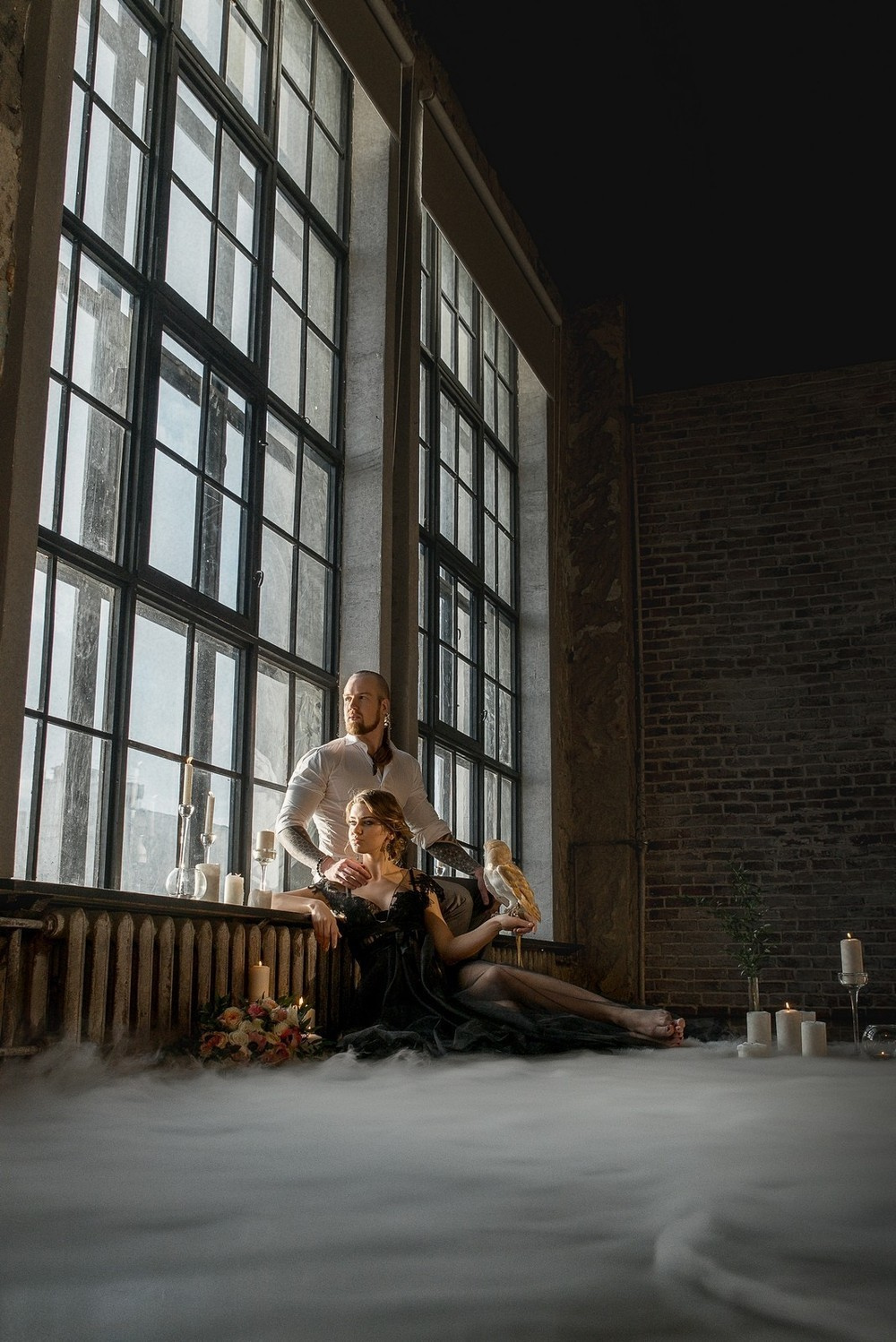 Общий план. невеста сидит у окна с совой на плече на фоне стоящего за ней жениха Свадебная фотосъемка в Москве. Свадебный фотограф в Москве Сергей Гаварос.