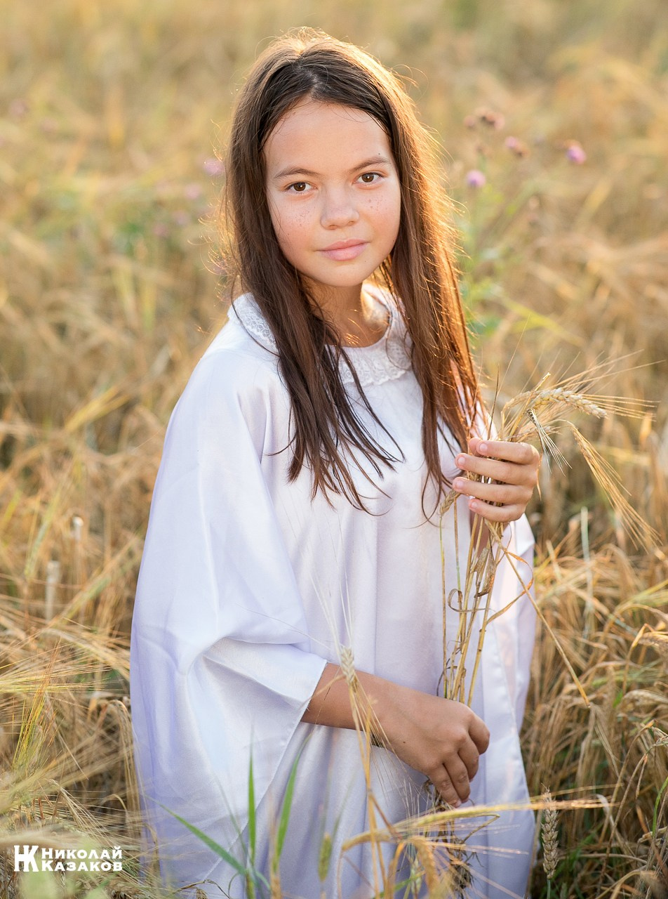 Портрет счастливой девочки в лучах закатного солнца во время фотосессии в пшеничном поле.