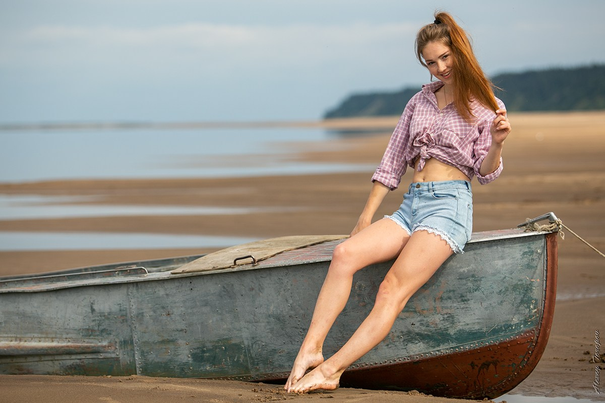 Девушка в шортах позирует на старой лодке на берегу реки