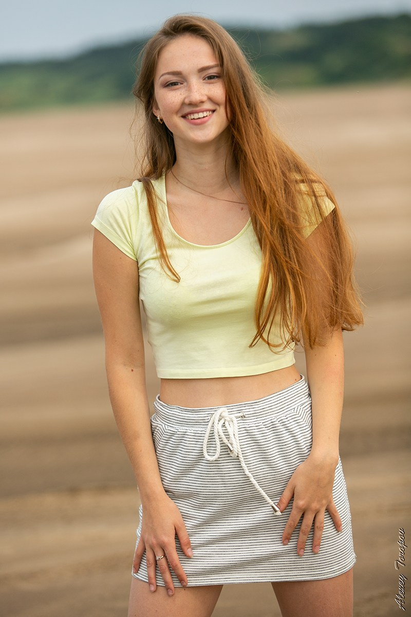 Юная девушка стоит на фоне песчаного берега