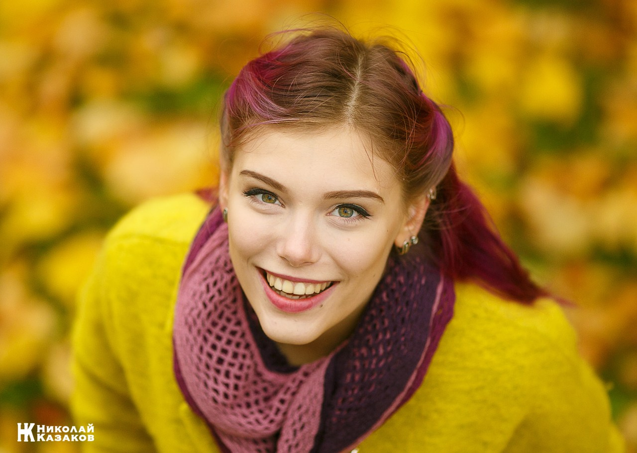 Позитивный портрет молодой женщины с улыбкой на лице на фоне размытых осенних листьев