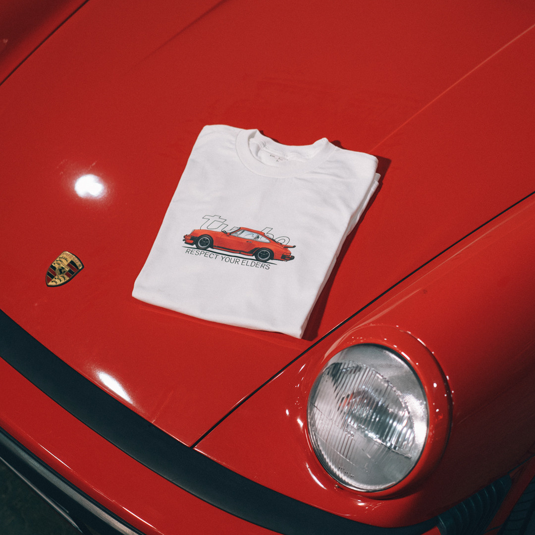 Классическая белая футболка лежит на капоте красного Порше 911