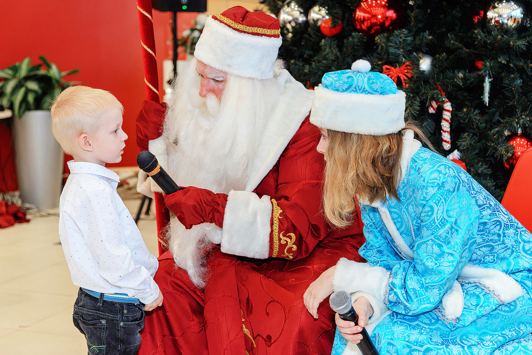 Мальчик возле новогодней ёлки читает стих Деду Морозу и Снегурочке.
