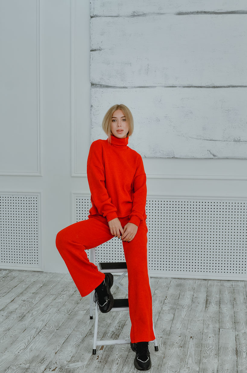 Модель, блондинка в красном, теплом костюме на светлом фоне в фотостудии.
