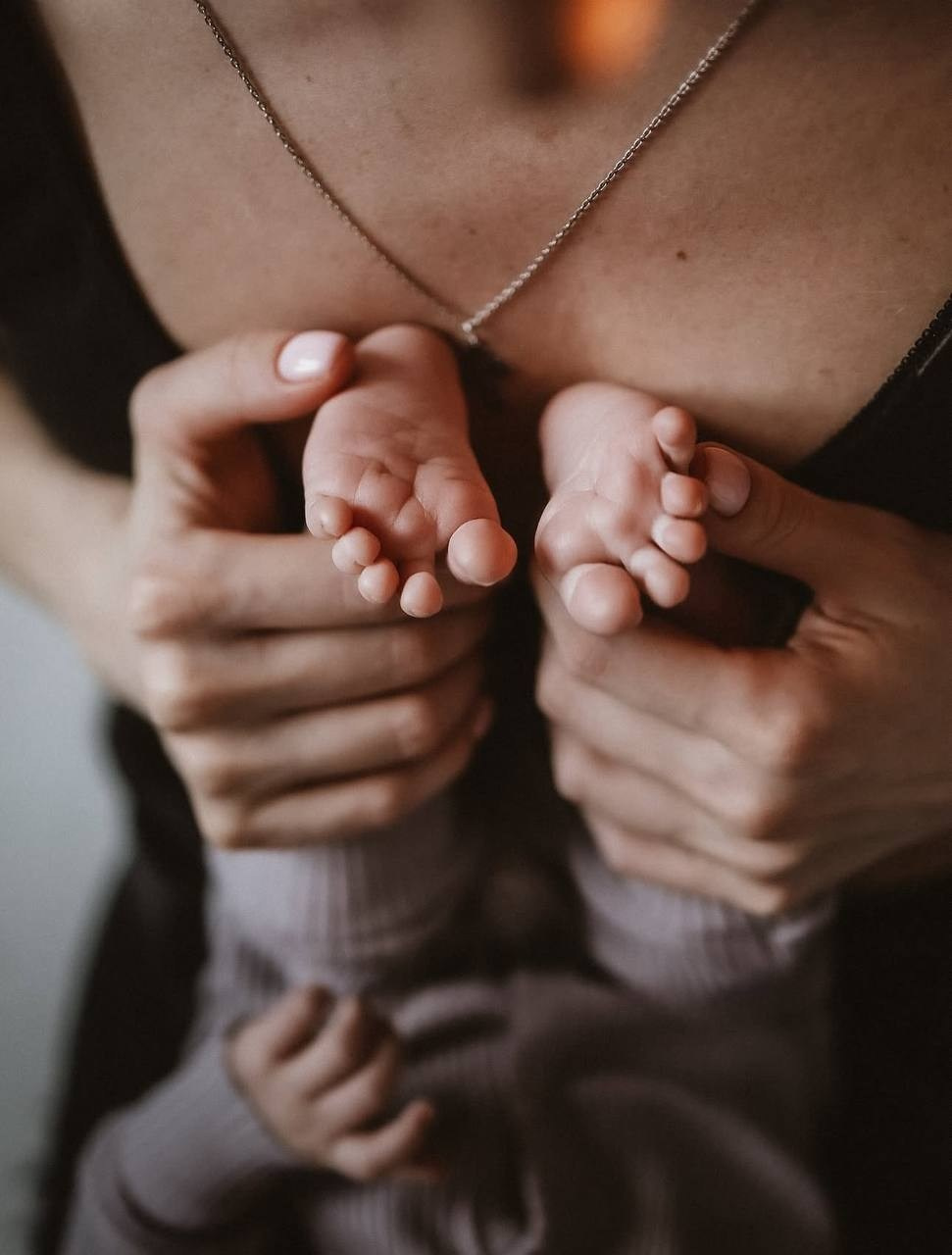 Мама аккуратно держит крошечные ножки малыша. Атмосфера очень тёплая, трогательная, домашняя.