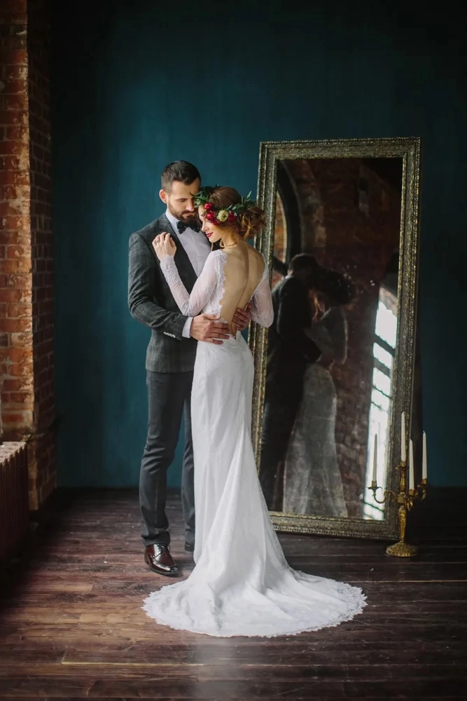 Жених и невеста стоят в обнимку на фоне ростового зеркала