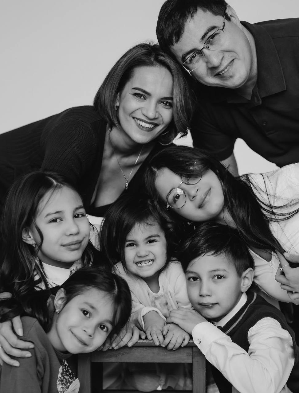Счастливая семья — мама, папа, четверо детей. Все улыбаются, тесно собрались вместе. Фотография в черно-белом стиле.