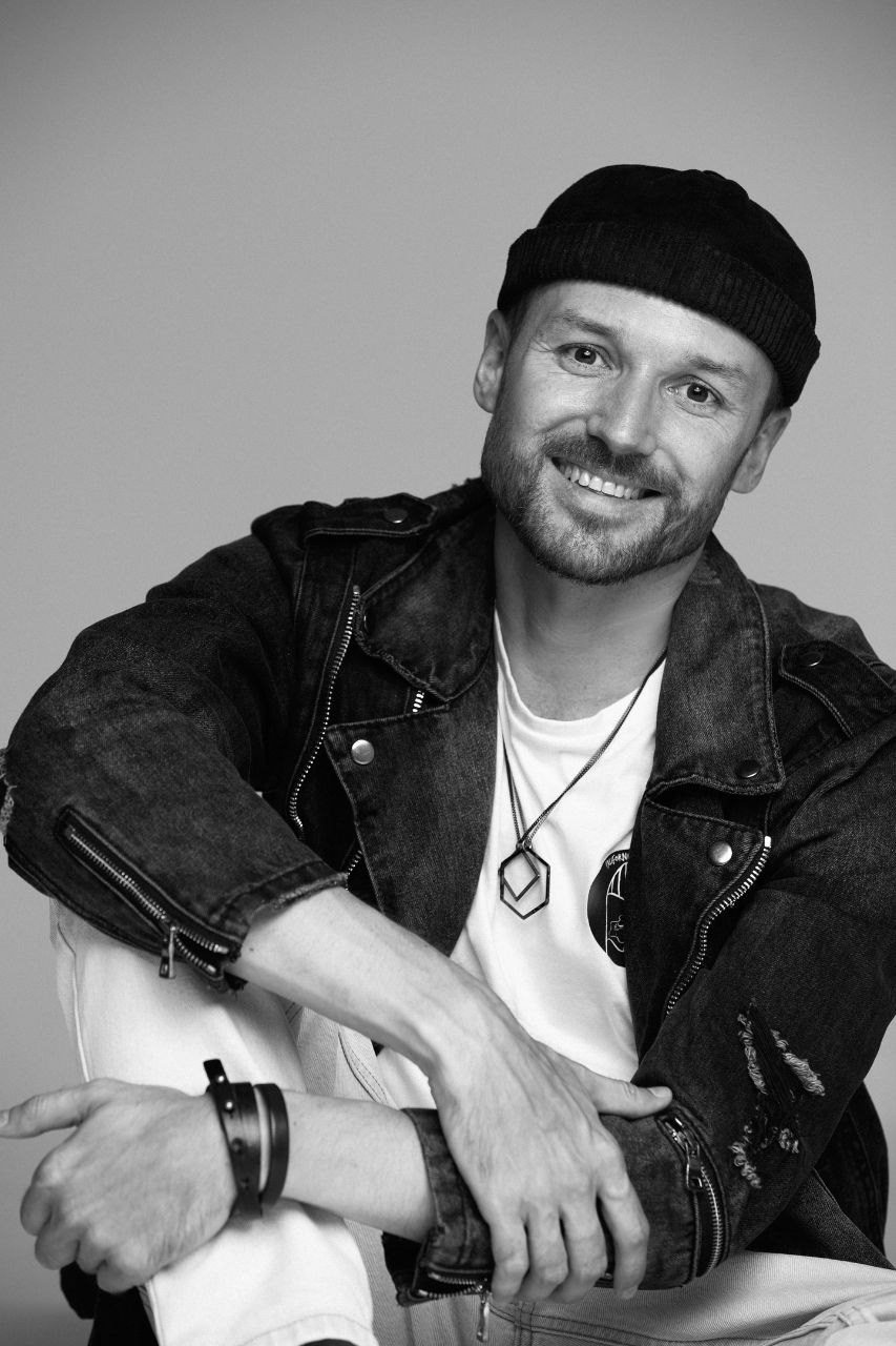 Мужчина с короткой щетиной в шапке и джинсовой куртке улыбается