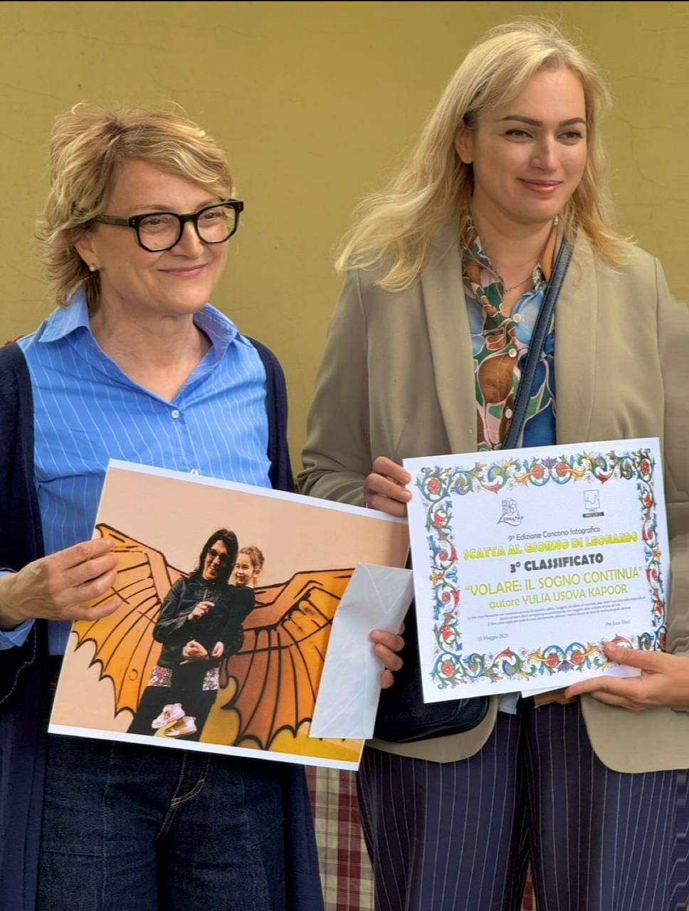 Юлия Перфетти держит сертификат в рамке и отпечаток победной фотографии «VOLARE: IL SOGNO CONTINUA» фотоконкурса «NATALE AMICO DI LEONARDO».