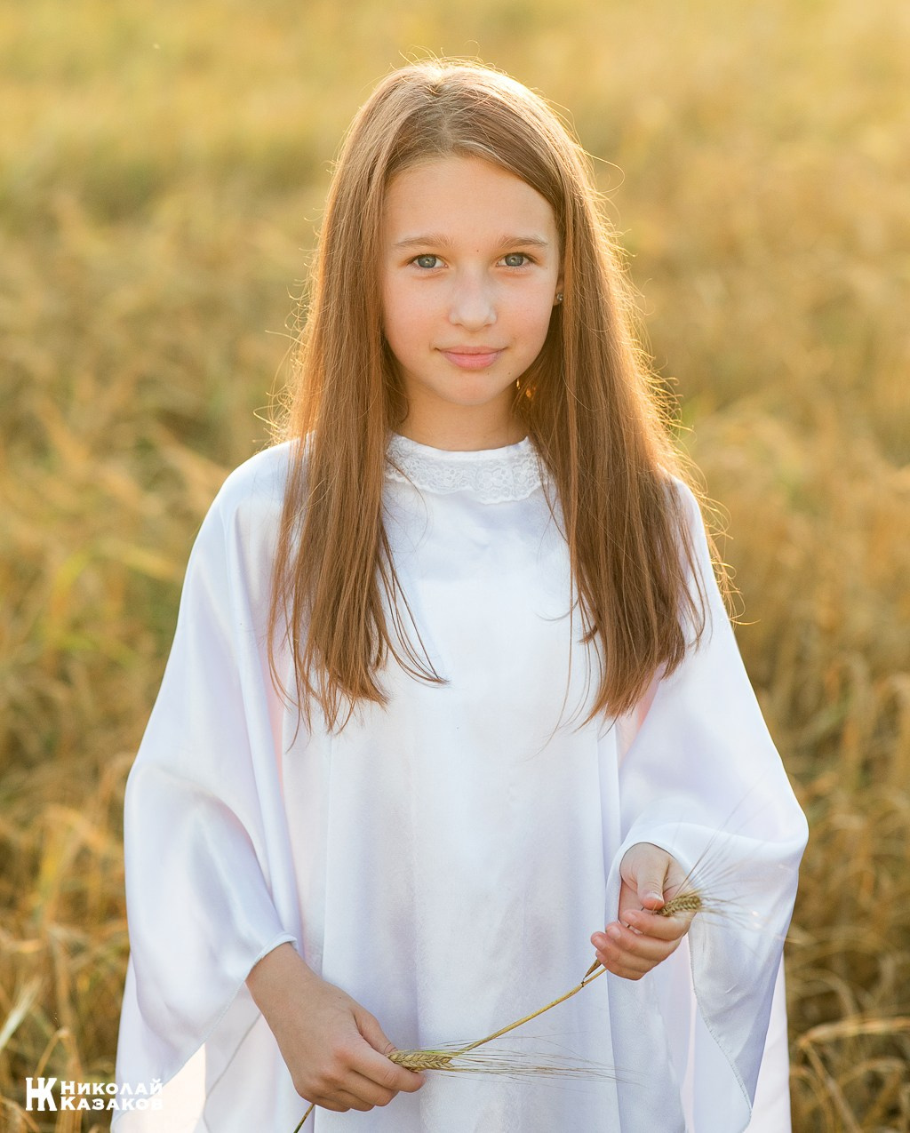 Портрет счастливой девочки с венком на голове в лучах закатного солнца во время фотосессии в пшеничном поле.