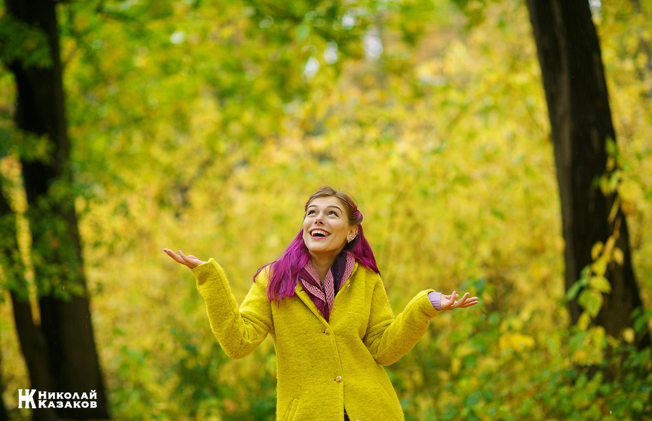 Жизнерадостная девушка смотрит в небо на фоне разноцветной осенней листвы