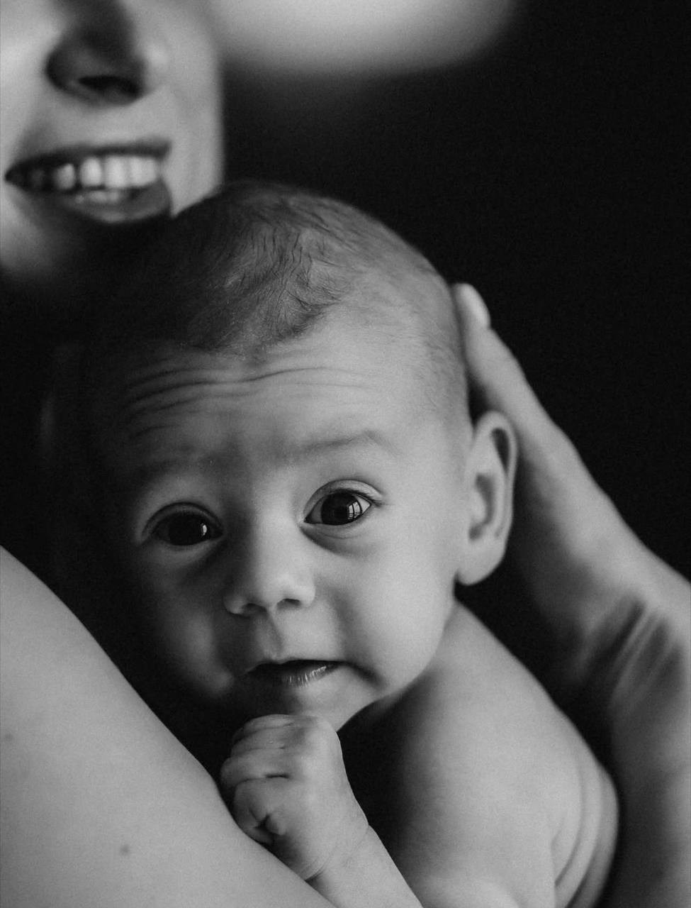 Мама держит на руках малыша, улыбается. Ребёнок с любопытством смотрит в камеру.