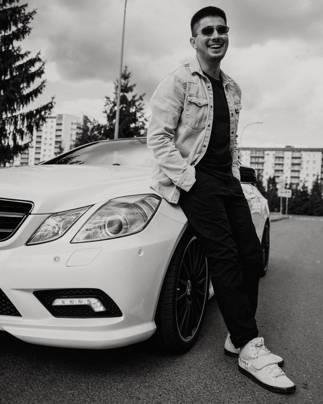 Ведущий Эмиль Белладжио позирует на фоне белого Mercedes возле Телецентра. Стильная чёрно-белая фотосессия на улице.