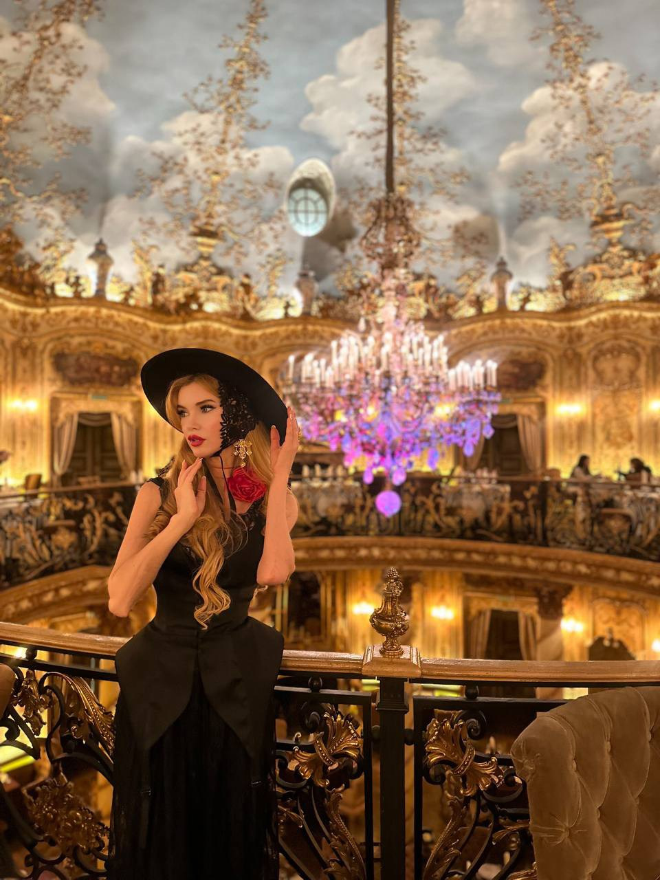 Портрет женщины в черной шляпе с красным цветком на шее на фоне люстры в основном зале ресторана Турандот