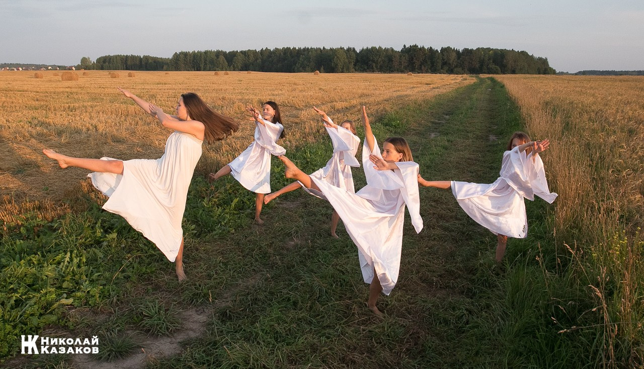 Стройные девочки подростки танцуют в пшеничном поле во время фотосессии на закате.