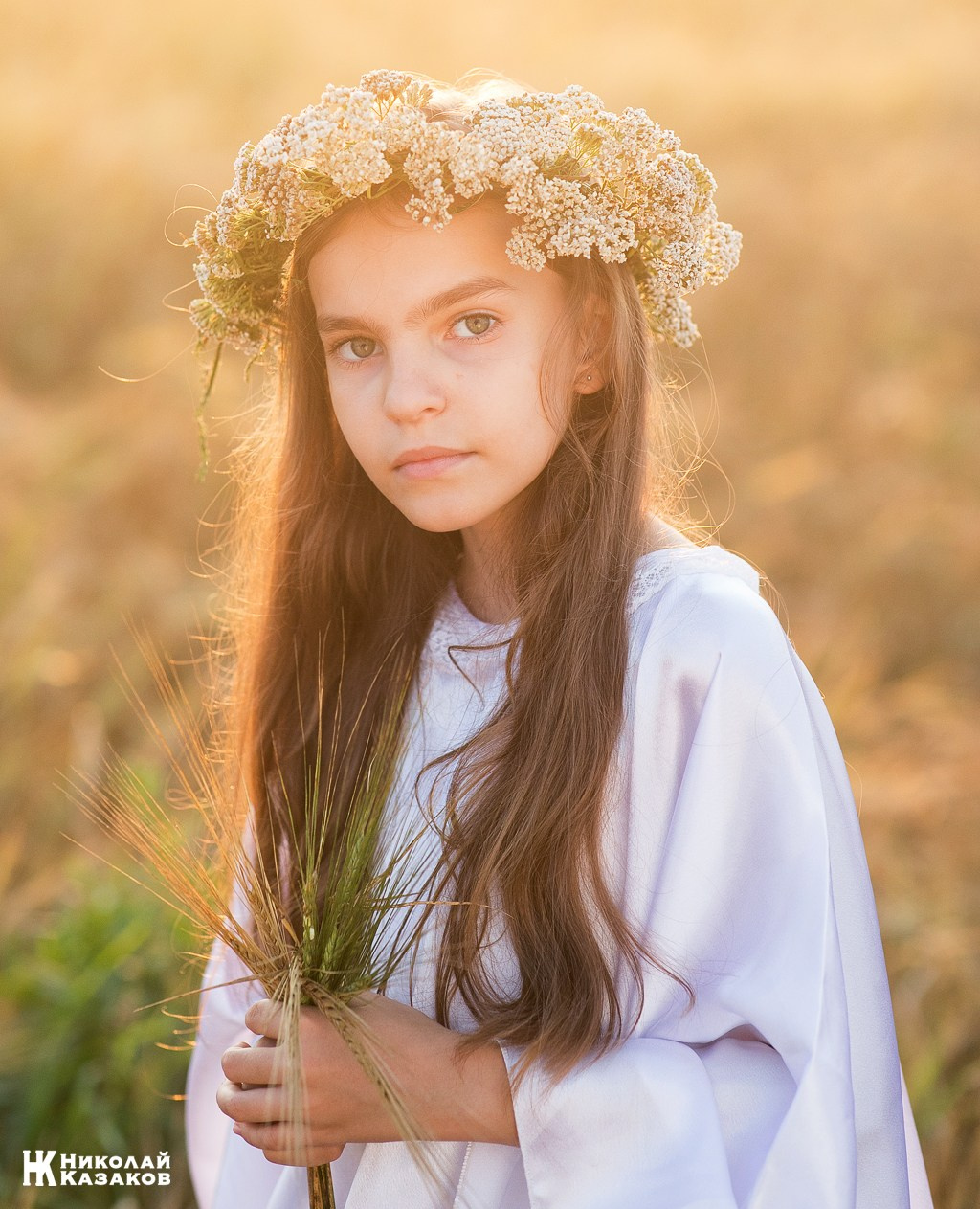 Портрет счастливой девочки с венком на голове в лучах закатного солнца во время фотосессии в пшеничном поле.